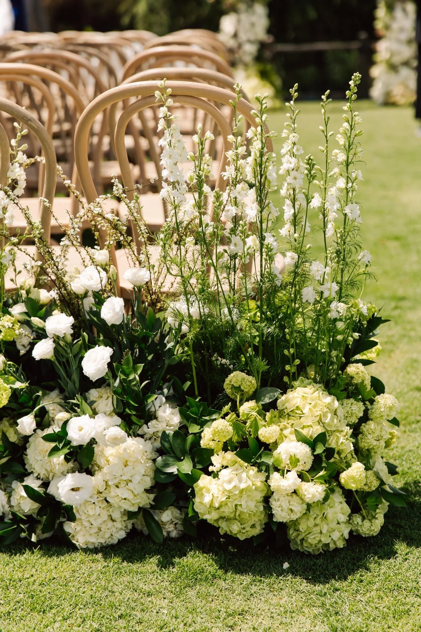 White floral arrangements with chairs in the background, likely at an outdoor wedding or event.