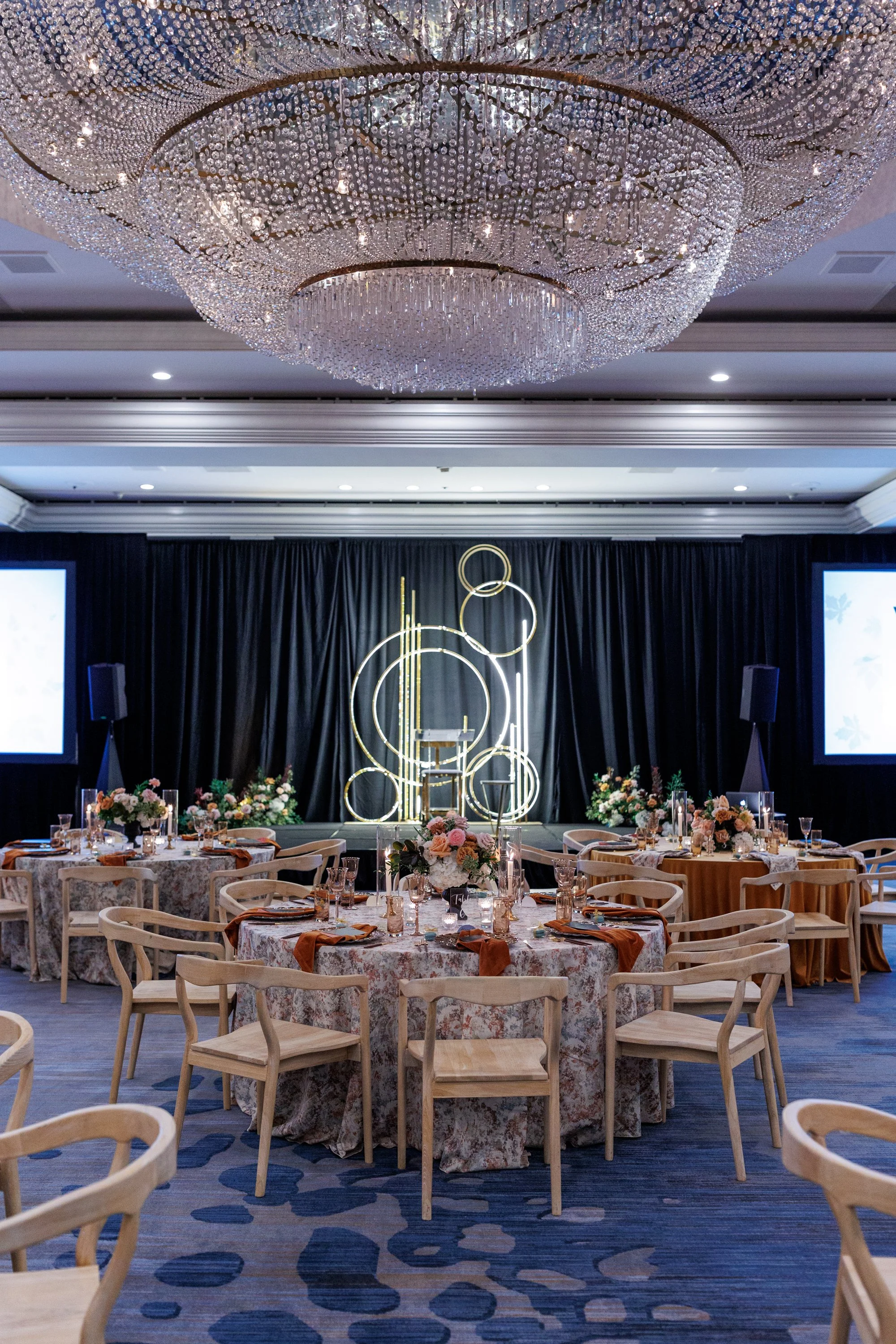 Ballroom wedding reception setup at Renaissance Newport Beach Hotel featuring fall-toned florals, layered linens, and modern stage design