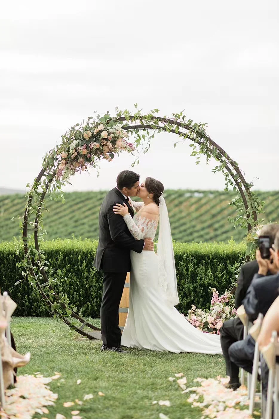 Bride and groom kissing under floral ceremony arch overlooking vineyard at Callaway Winery Temecula