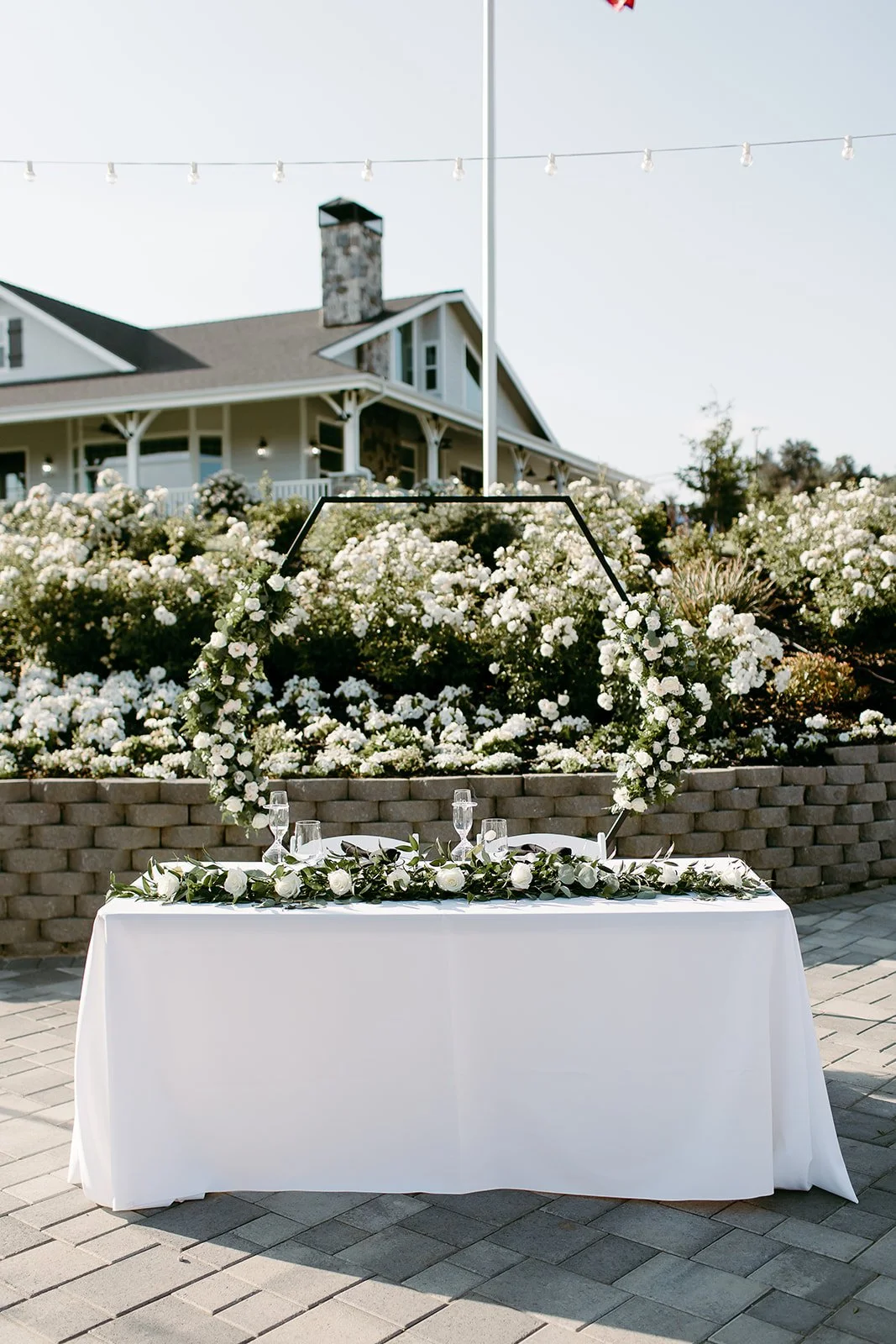 Outdoor estate wedding ceremony setup with sweetheart table, floral arch, and garden backdrop