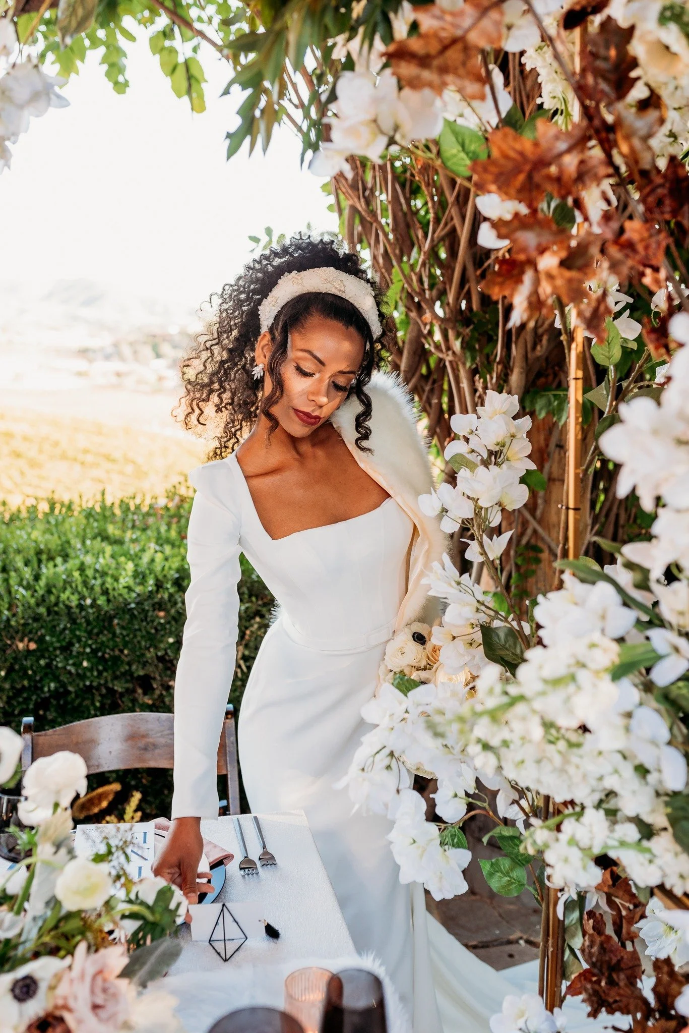 Bride standing near floral ceremony arch at South Coast Winery vineyard wedding in Temecula with sunset lighting