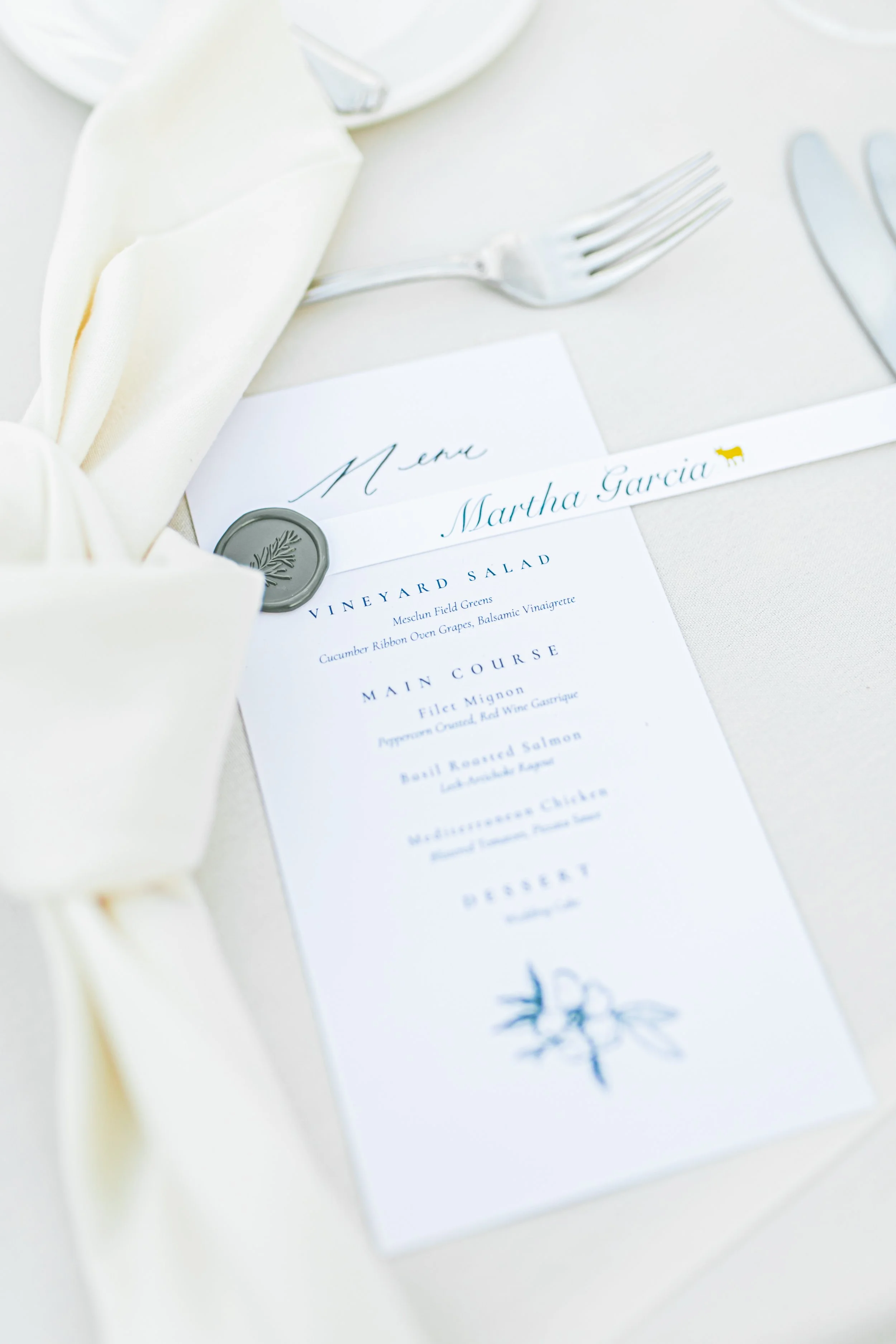 Wedding menu card with Martha Garcia's name, placed on a table with silverware, a napkin, and a wax seal.