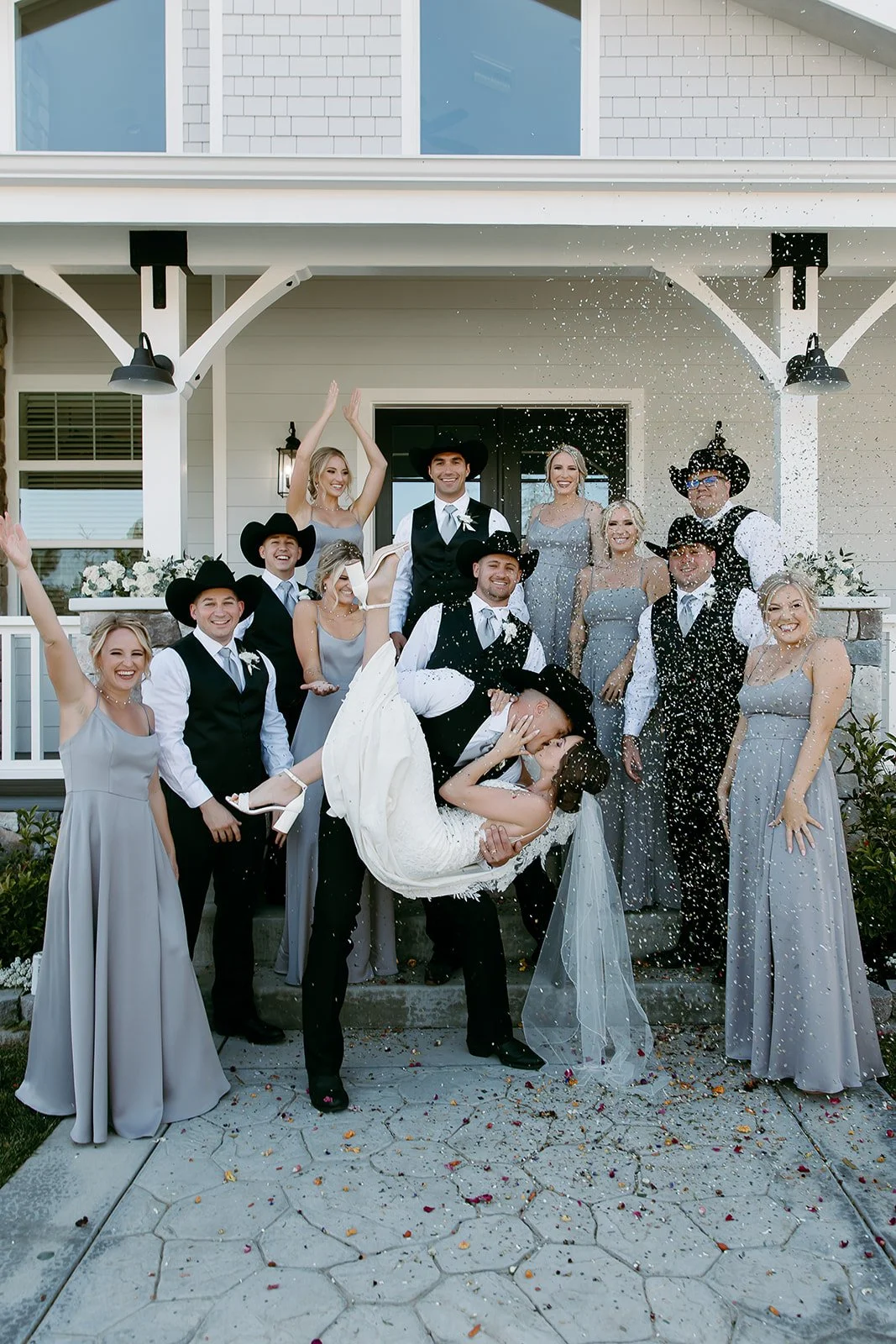 Bride and groom celebrating with wedding party outside private estate home with confetti toss