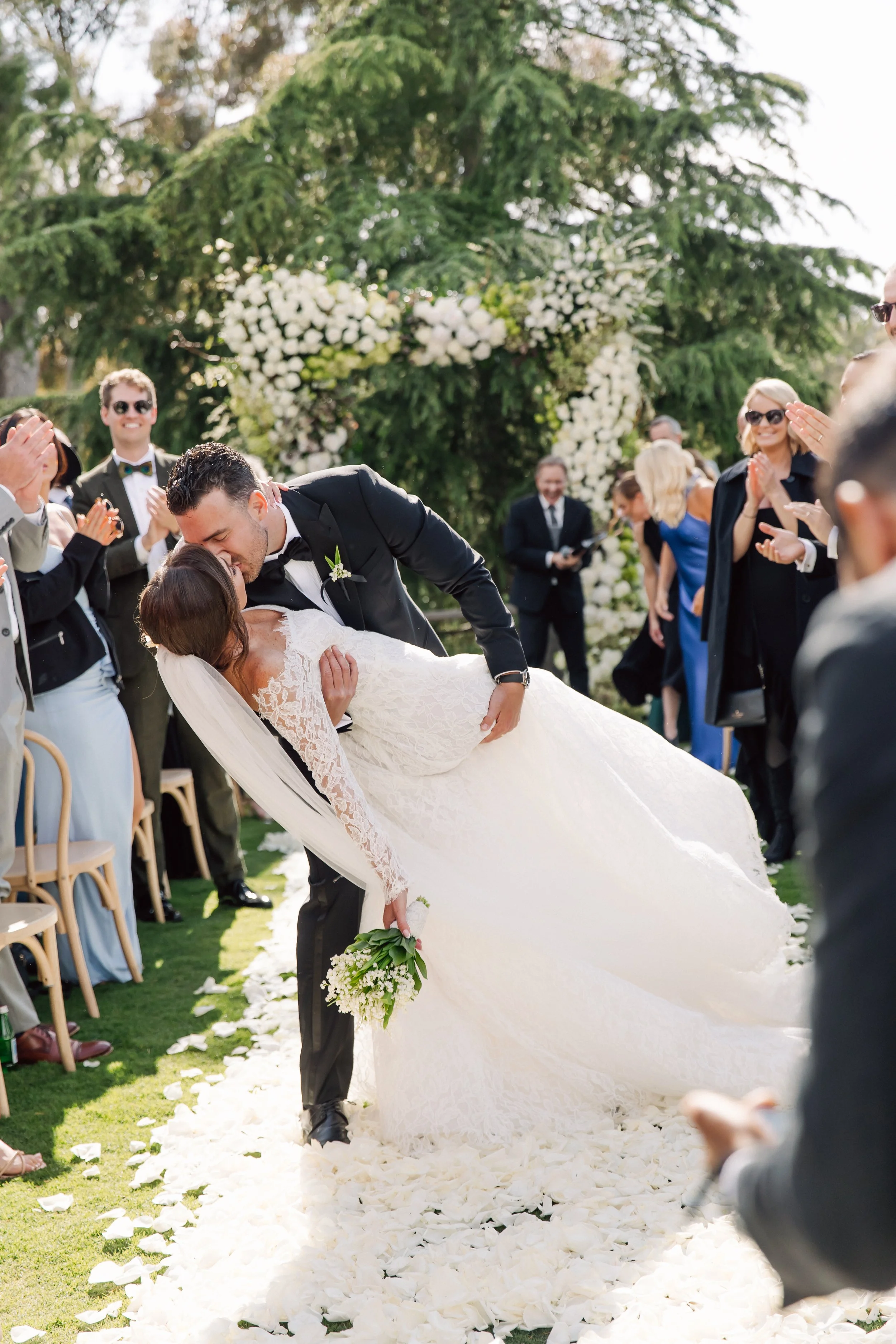 Bride and groom first kiss at private estate wedding ceremony in Rolling Hills Estates surrounded by guests and floral arch
