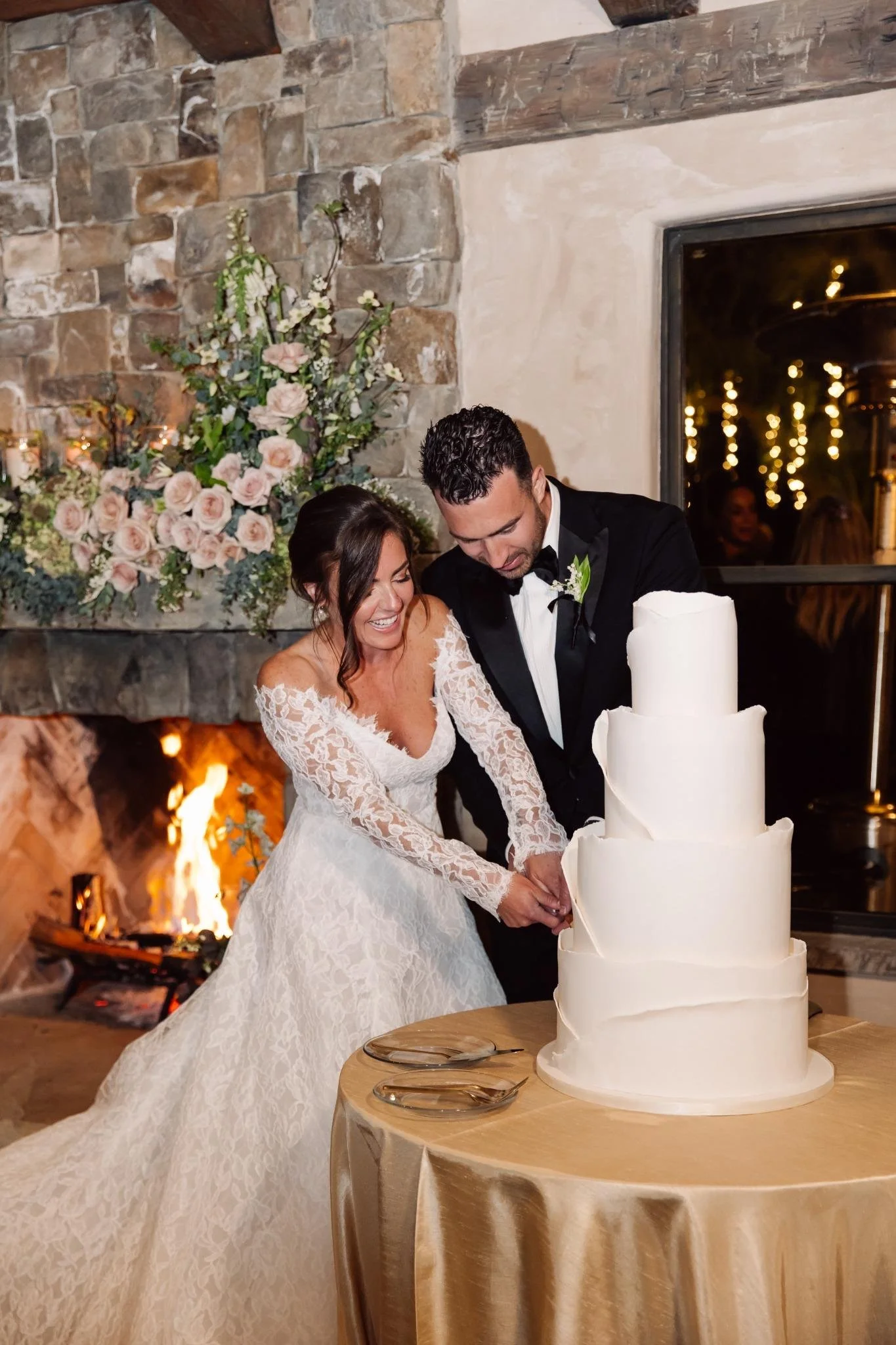 Bride and groom cake cutting at private estate wedding in Rolling Hills Estates with lush florals over fireplace.