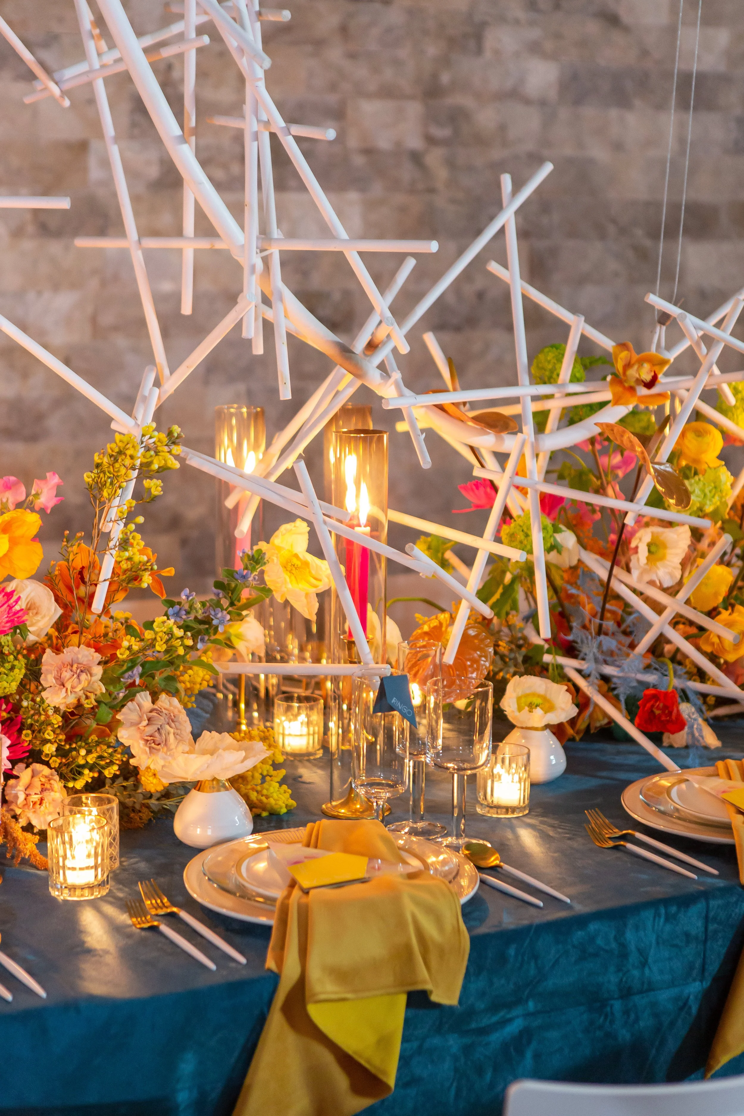 A decorated banquet table with candles, colorful flowers, and a modern white sculpture centerpiece, set for a special occasion. A Fete the Venue Wedding.
