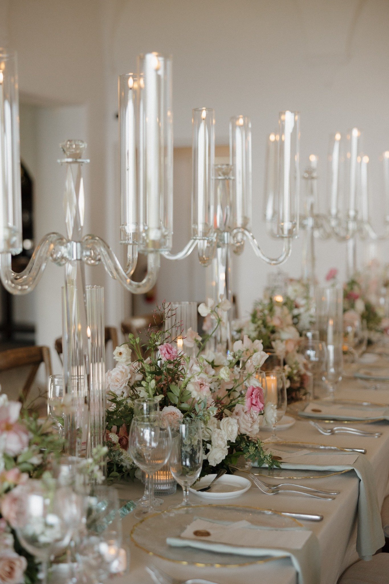 Elegant table setting with floral centerpieces, tall glass candelabras, and place settings including glassware and napkins for a formal event.