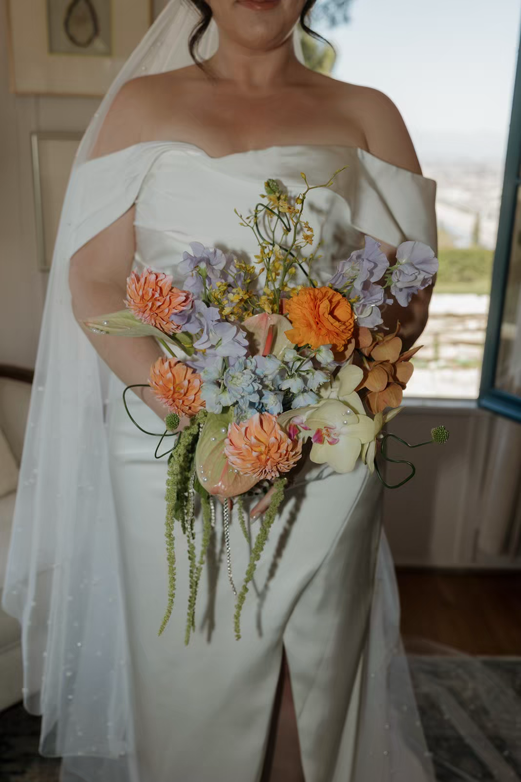 a bride dressed in white holds a colorful jeweled bridal bouquet with bright blue orange and pink flowers