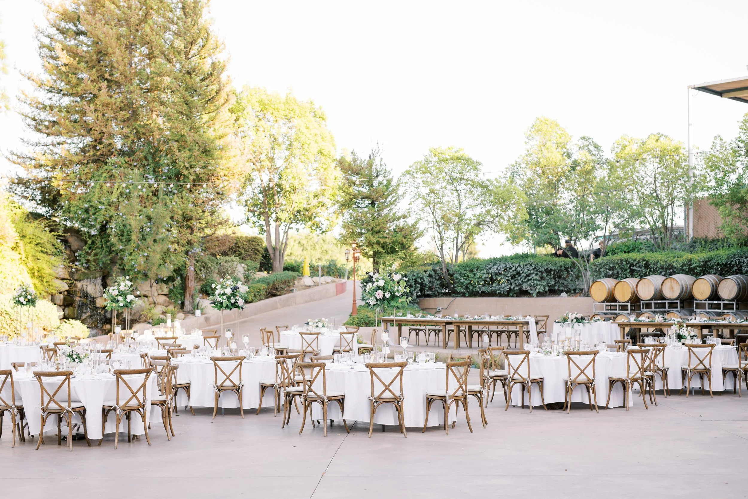 Reception photo with brown wooden cross back chairs, brown farmhouse tables, and circle white linen tables with tall floral centerpieces