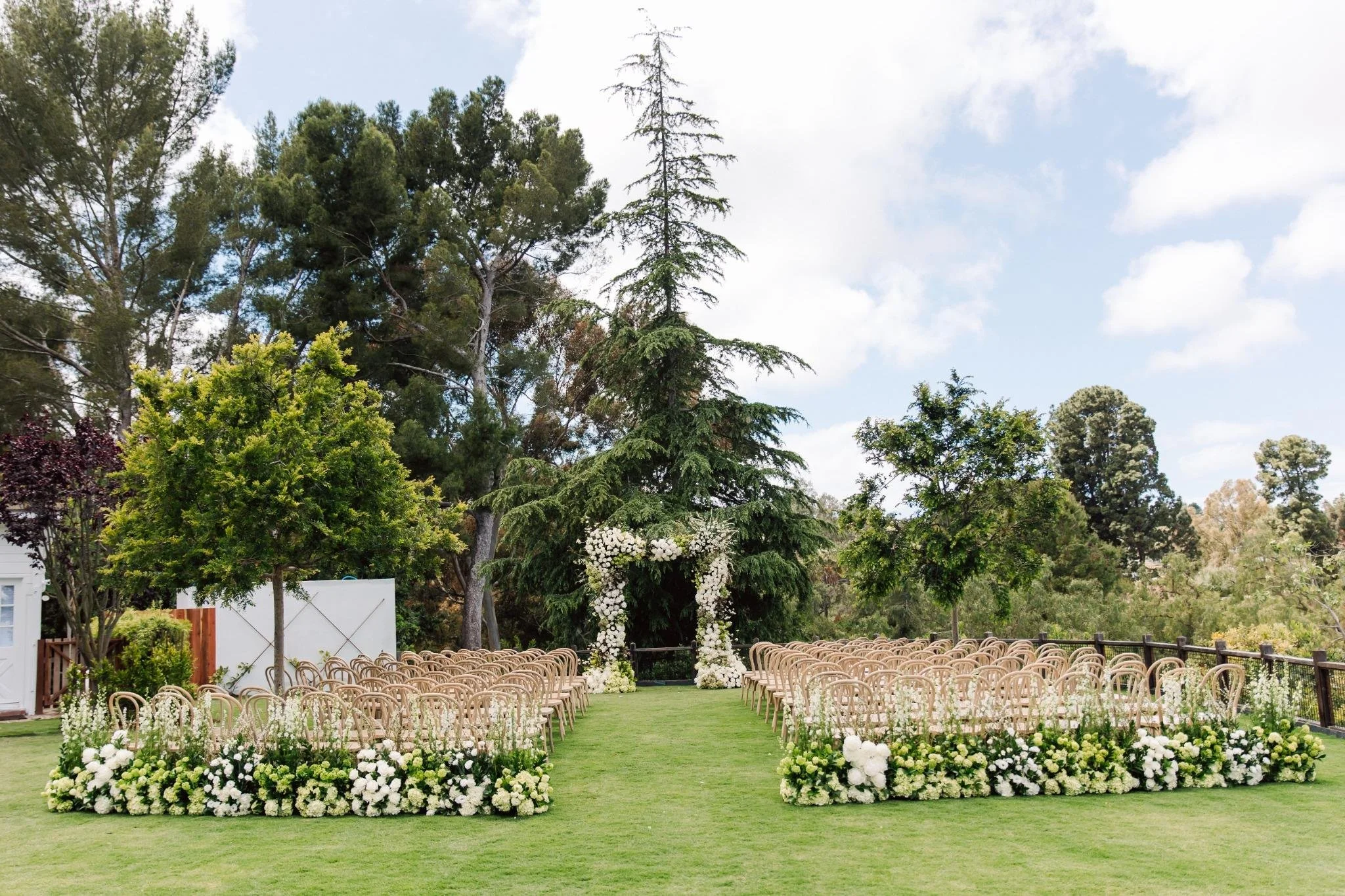 Wide view of outdoor ceremony setup at private estate wedding in Rolling Hills Estates with wooden chairs and garden setting