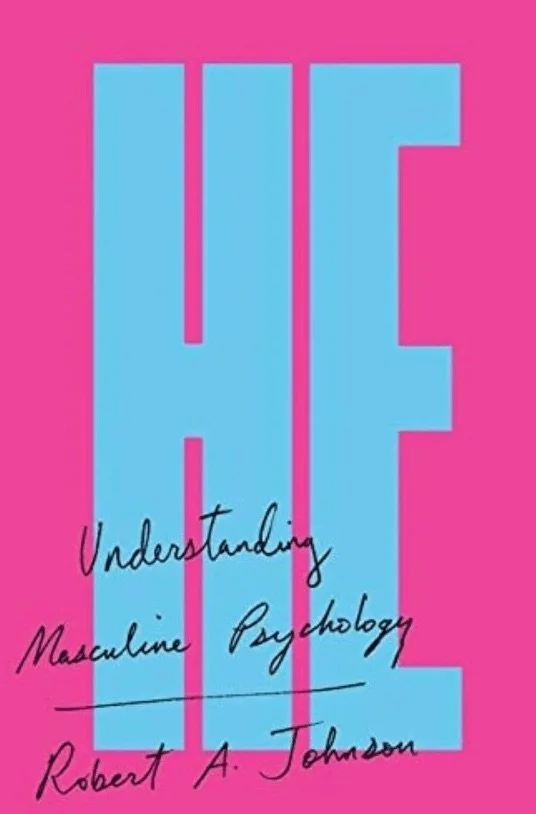A pink background with large blue letters spelling 'HEF'. Over the letters, there is black handwritten text that reads 'Understanding Masculine Psychology' and the author's name, Robert A. Johnson.