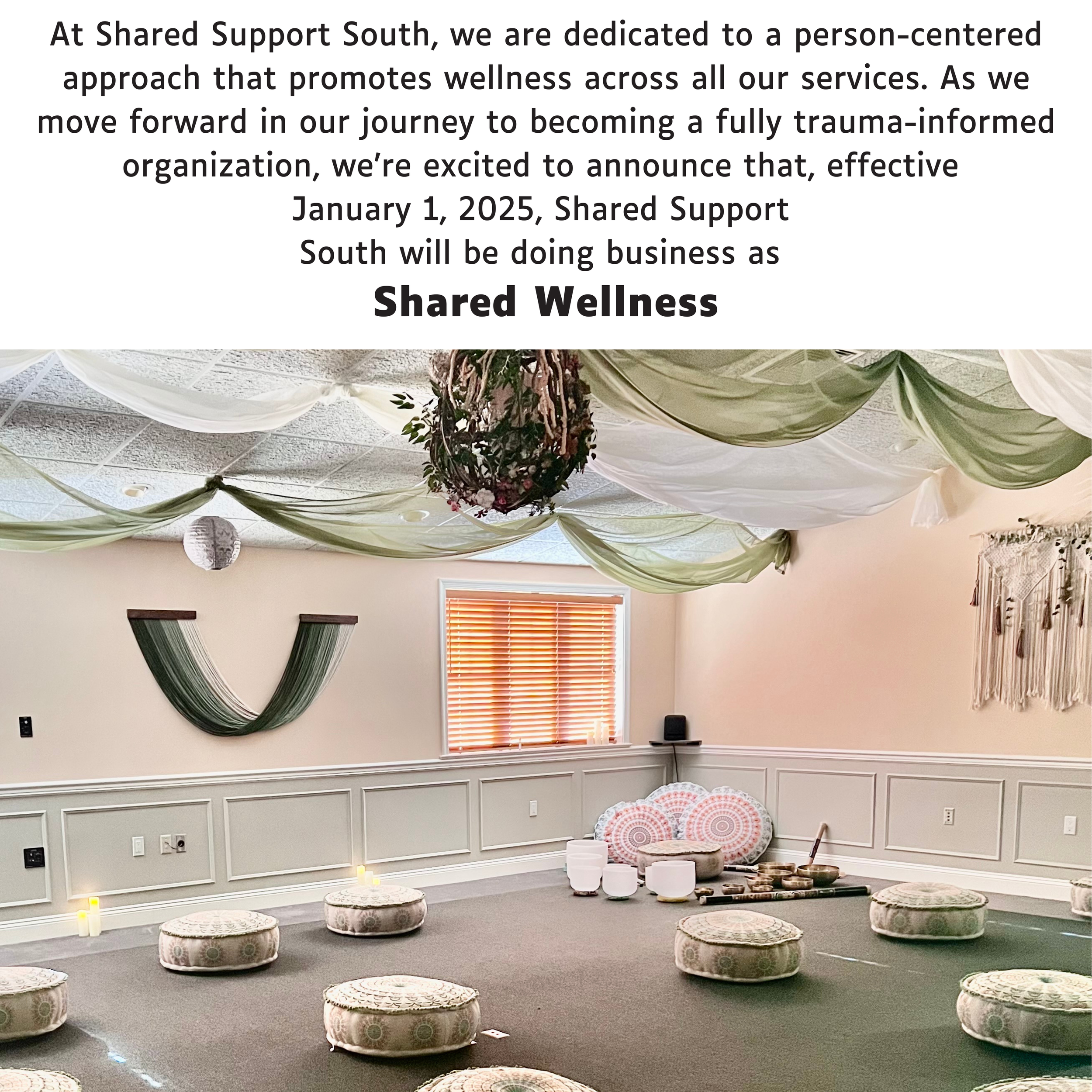 Interior of a wellness room with meditation pillows, decorative drapery on the ceiling, circular floor cushions, and musical instruments. A notice above announces Shared Support South's rebranding to Shared Wellness from January 1, 2025.