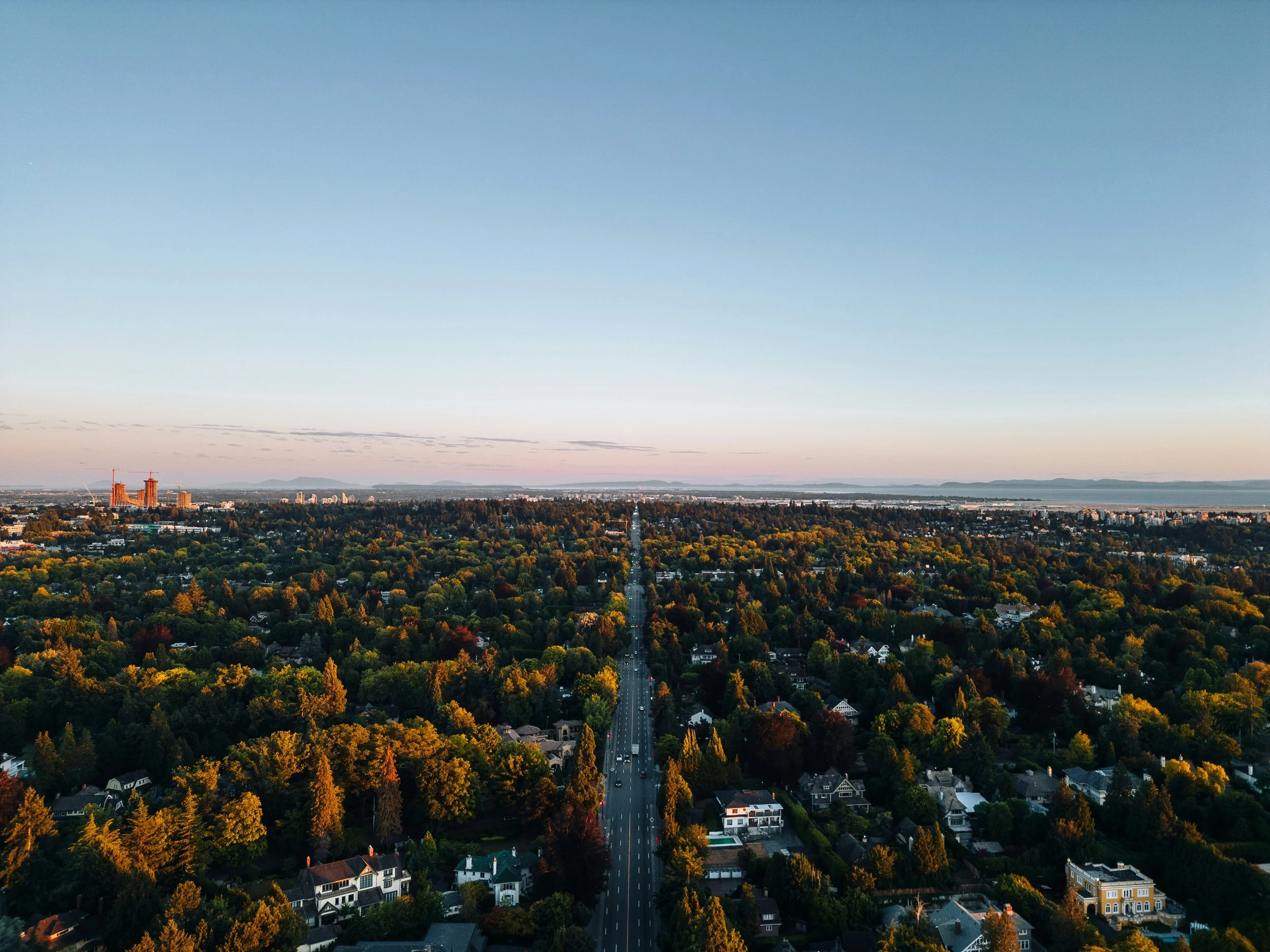 A view overlooking a BC suburb during a summer sunset with highrise construction in the background set in front of the pacific ocean and distant mountains.