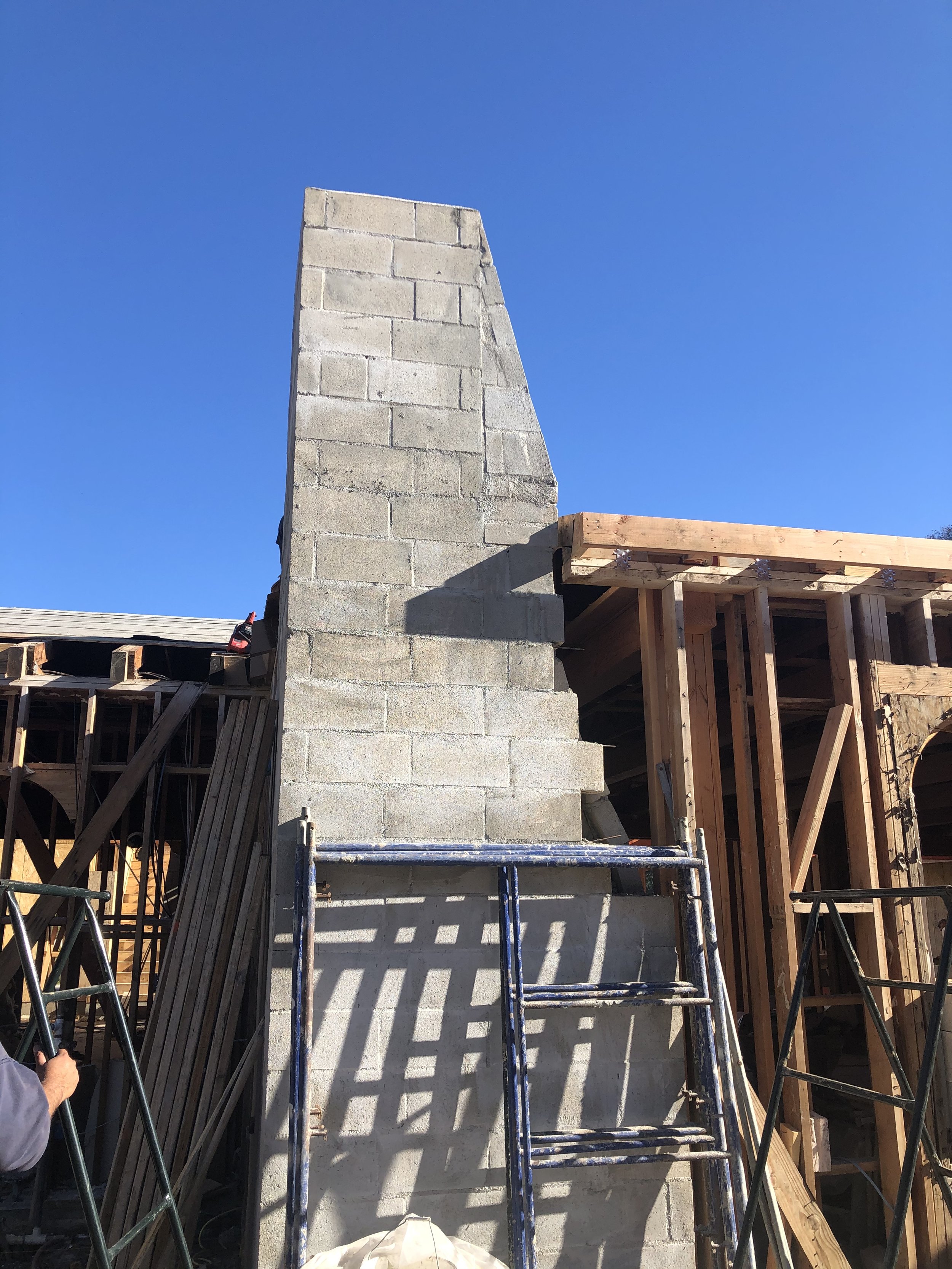 Construction site with a concrete chimney and wooden framework for a building under construction, with scaffolding and ladders.