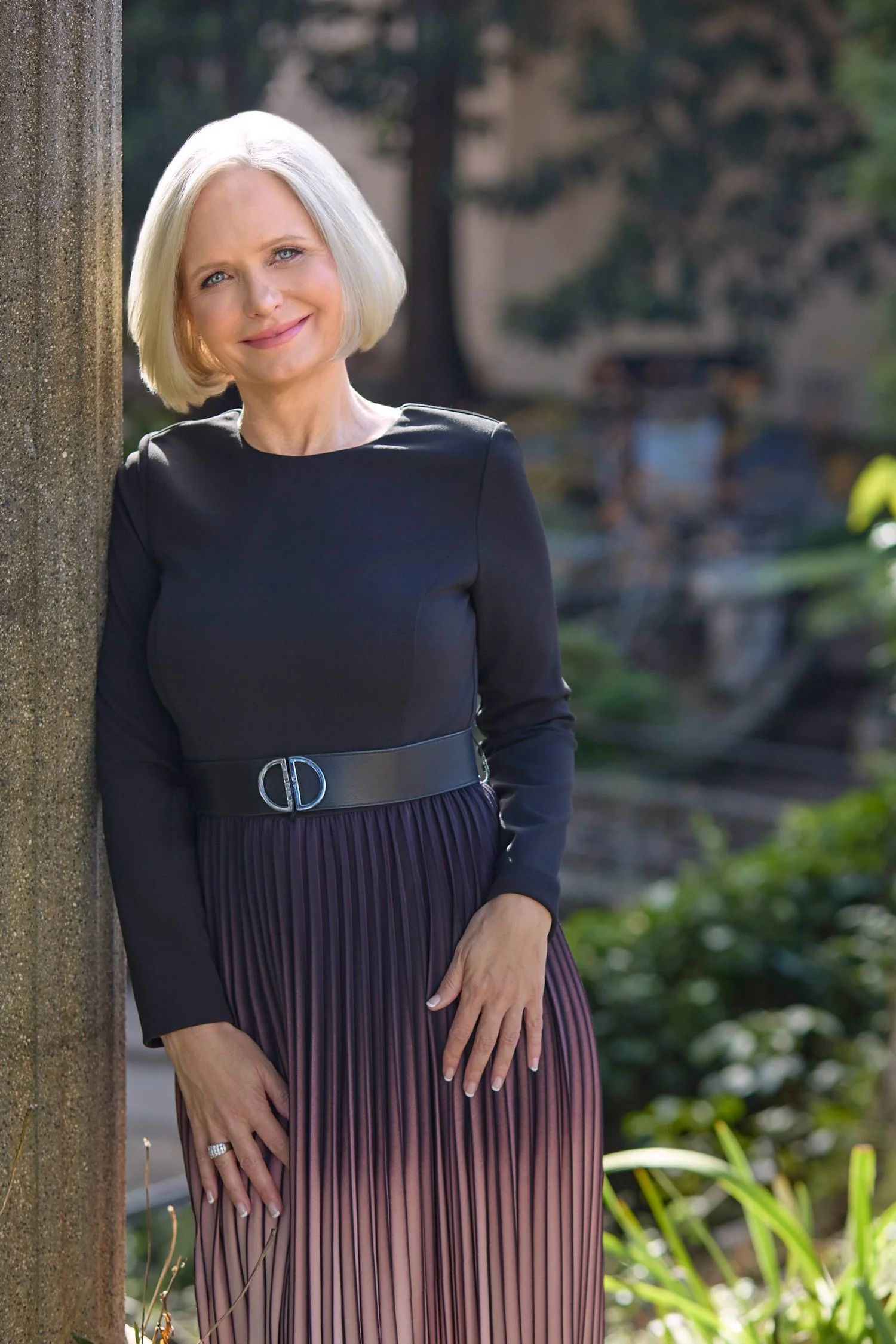 Beautiful woman in a park leaning against a light post smiling