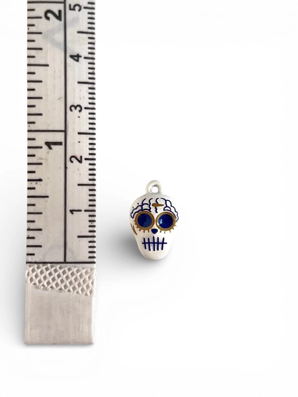 White enamel sugar skull charm with blue eyes and decorative detailing