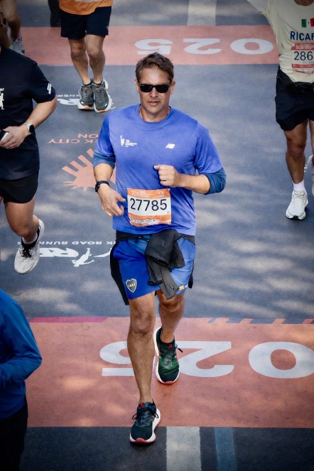 A man in blue running gear, wearing sunglasses and a race bib number 27785, participating in a marathon or race.