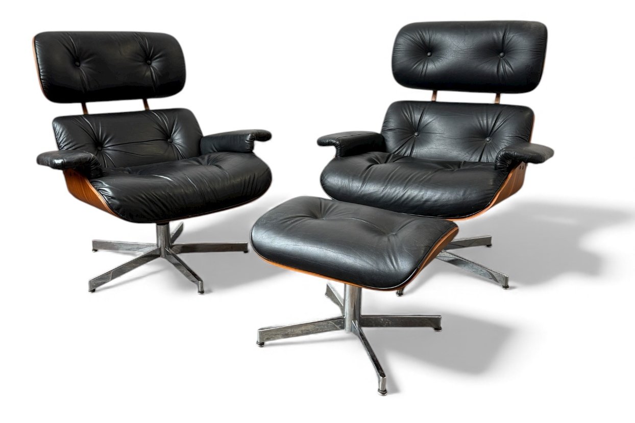 Two black leather lounge chairs with matching ottomans, featuring high backs and wooden accents, positioned on a white background.
