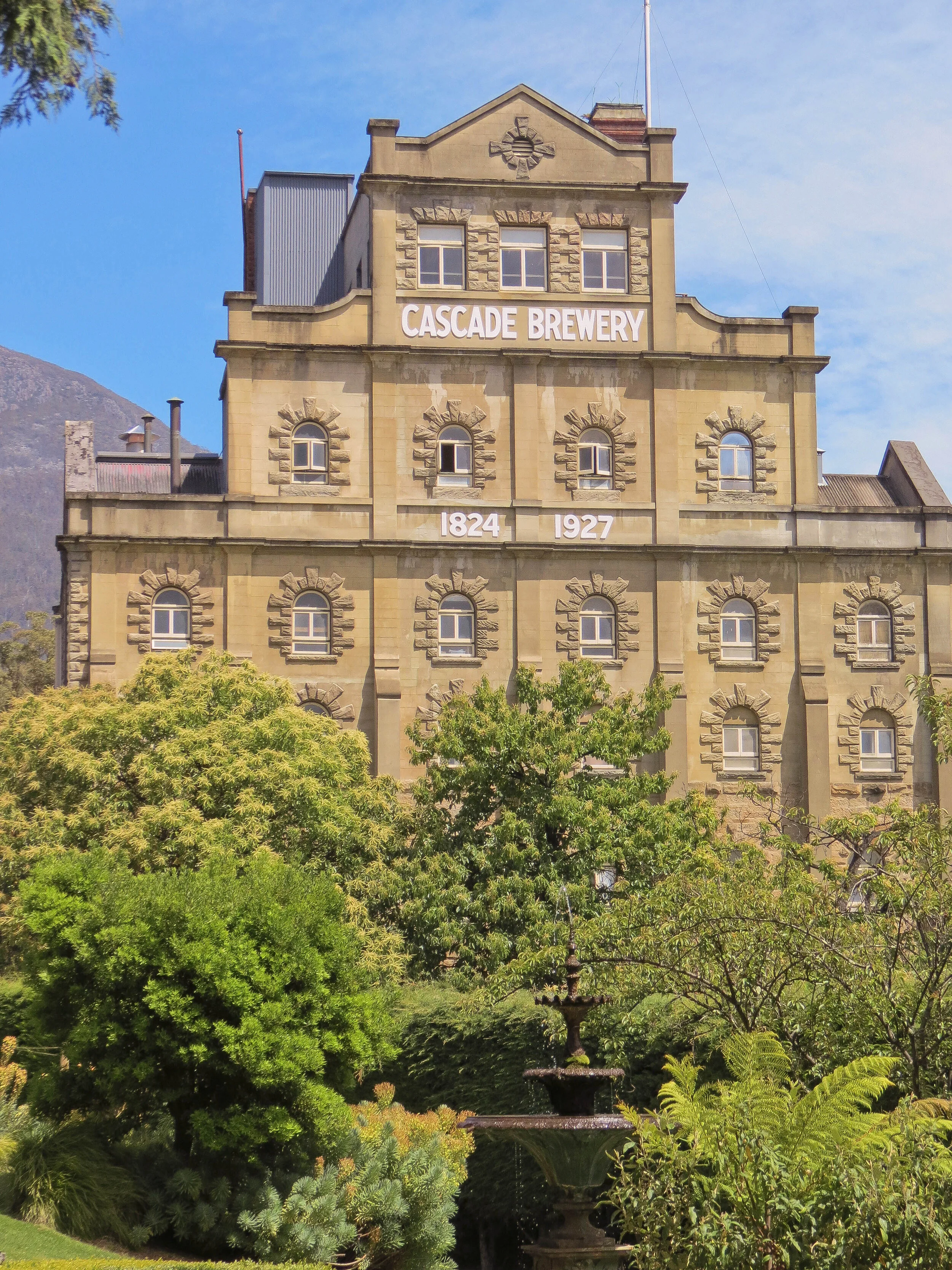 Historical building with sign 'Cascade Brewery', trees, and fountain in foreground.