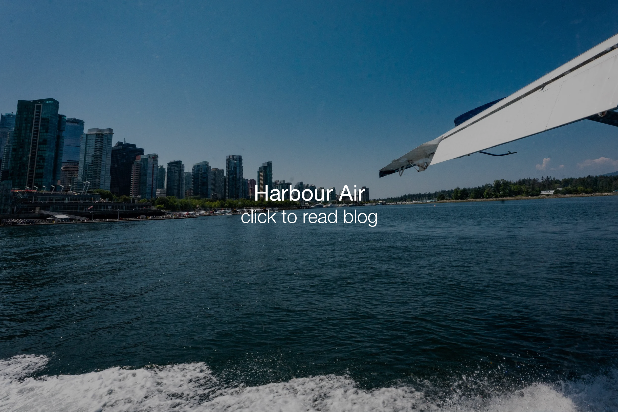 View of a city skyline from the water with a boat's wake at the bottom and a part of a boat's wing on the right side.