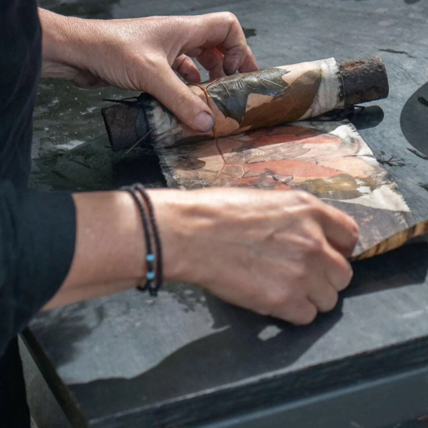 Hands carefully unrolling a textured, colorful map or artwork on a dark surface.