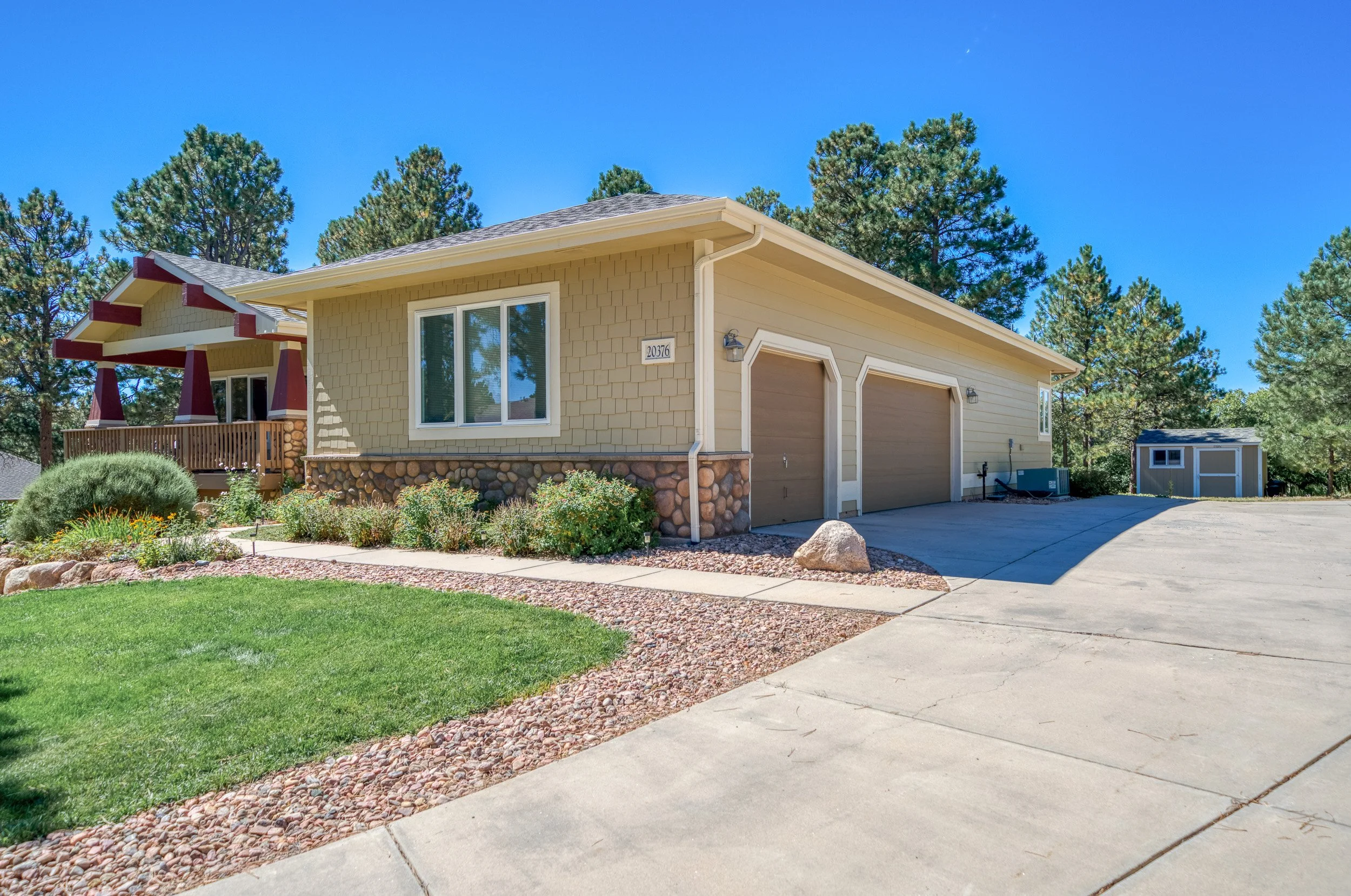 Suburban house with two-car garage, landscaped yard, and driveway, surrounded by trees.