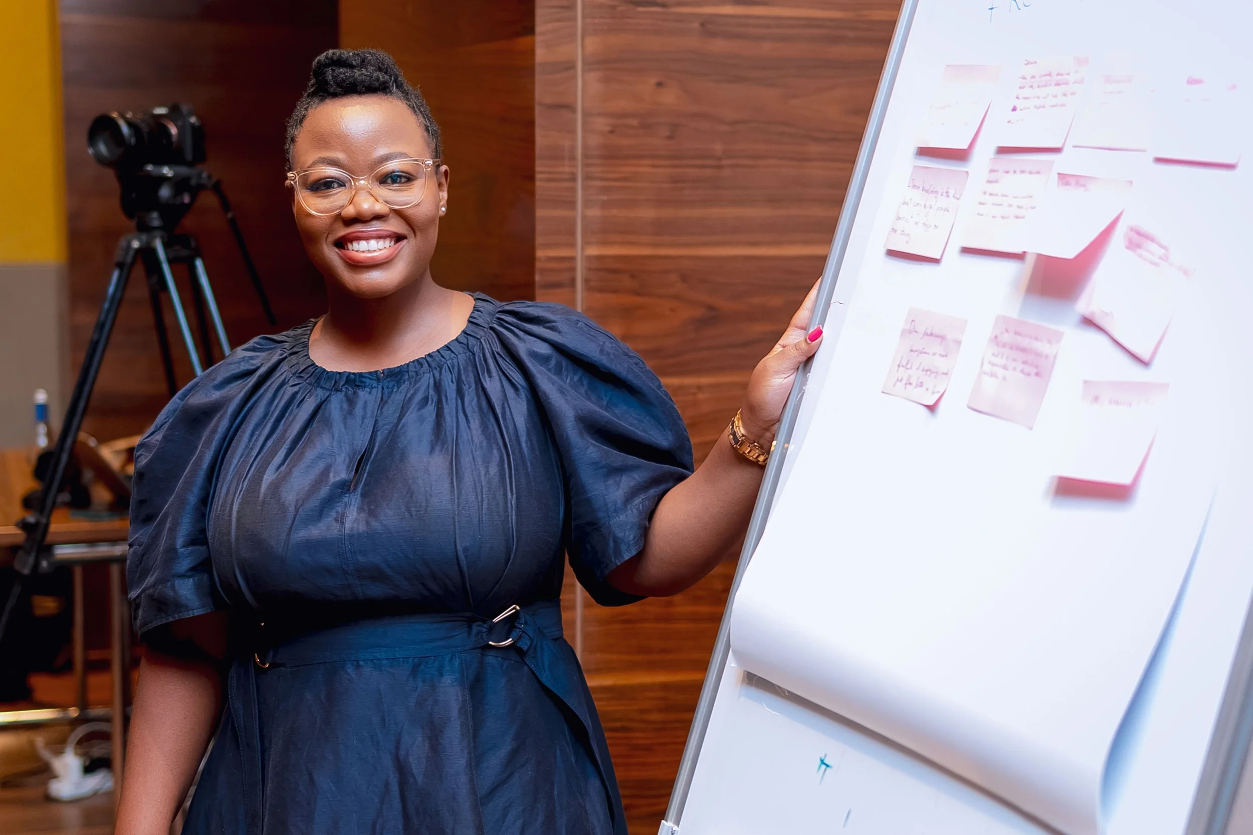 Woman with braided hair holding a microphone, standing near a whiteboard with writing.