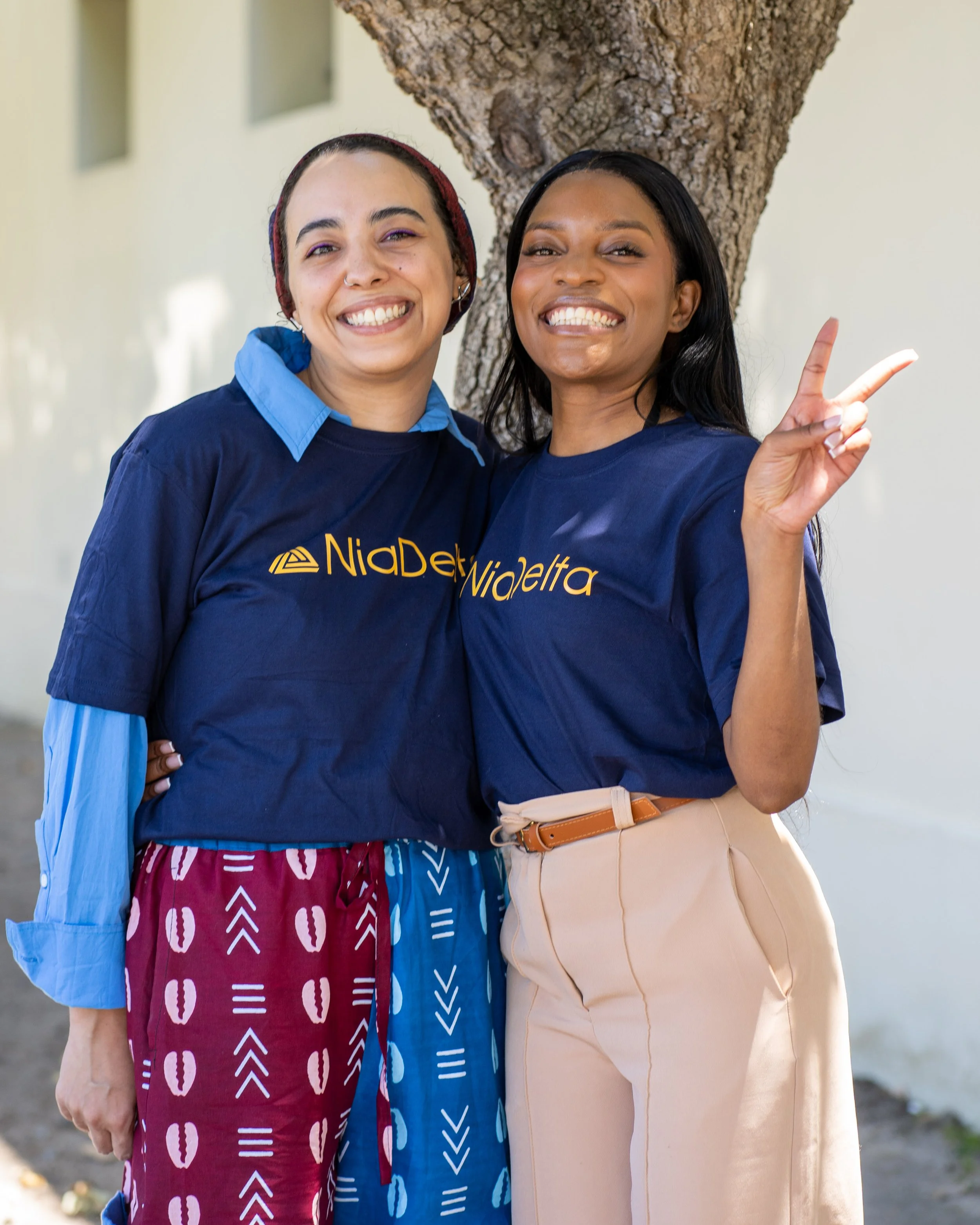Four people wearing "NiaDelta" logo t-shirts standing together outdoors.