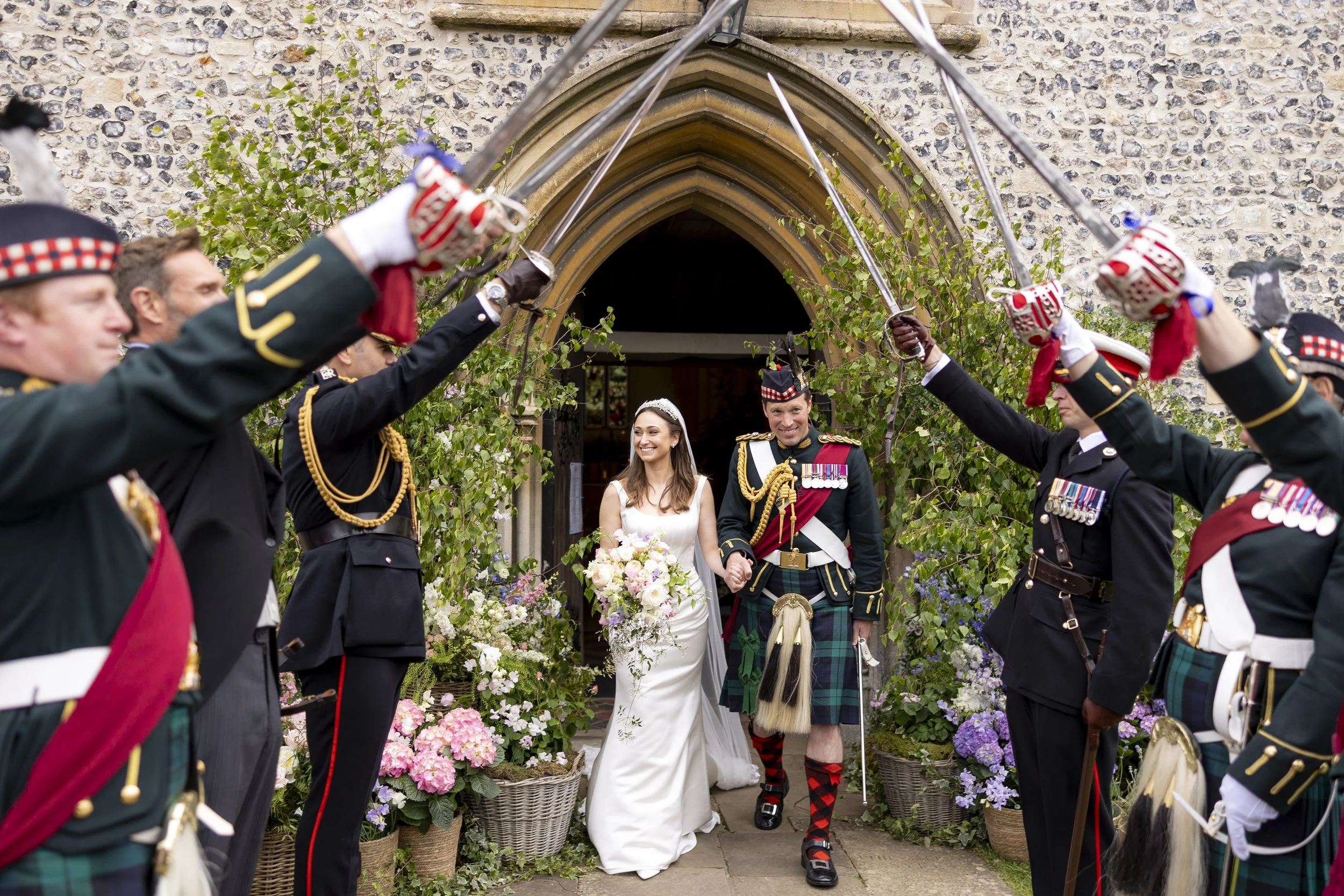 Bride and groom walking through a ceremonial archway surrounded by soldiers in traditional Scottish military uniforms for a wedding.