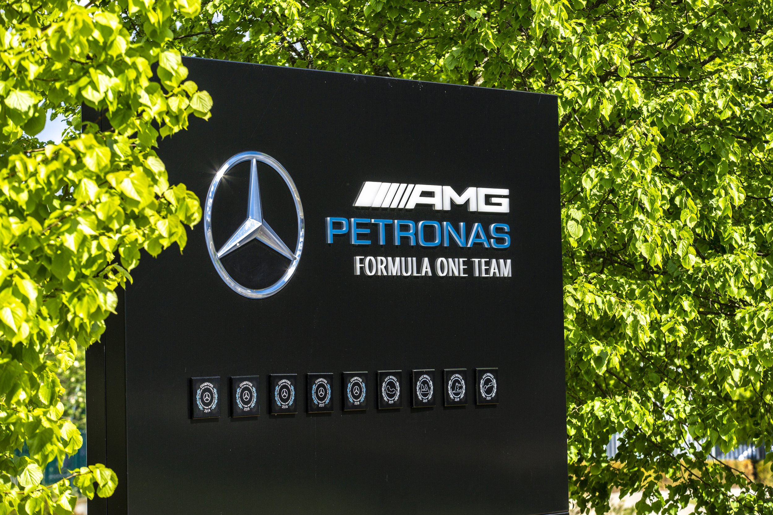 Mercedes-Benz AMG Petronas Formula One Team sign outdoors, with green trees in background.