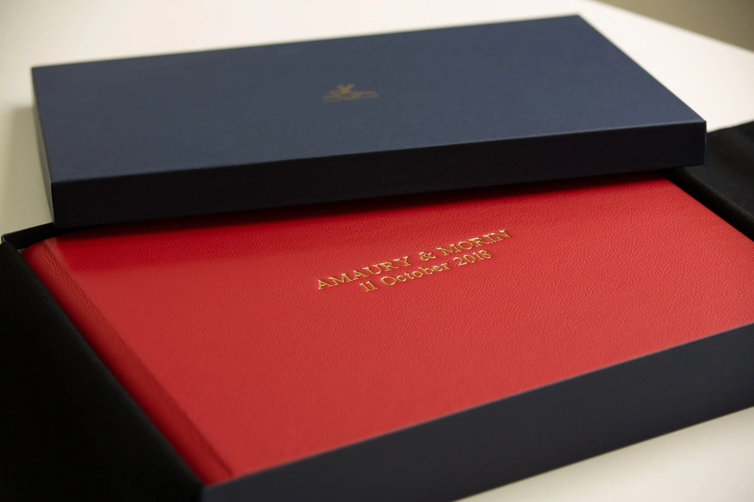 Red book with gold embossed text inside a black box, featuring names and a date.