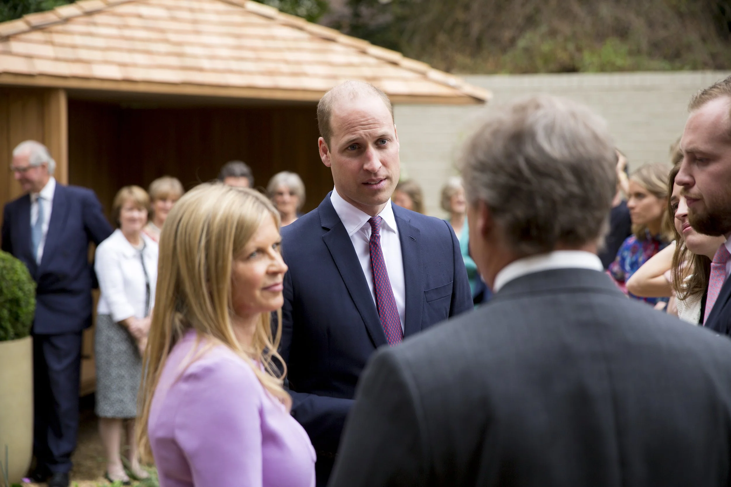 Prince William and Catherine, Duchess of Cambridge, at an outdoor event, engaging in conversation with several people.