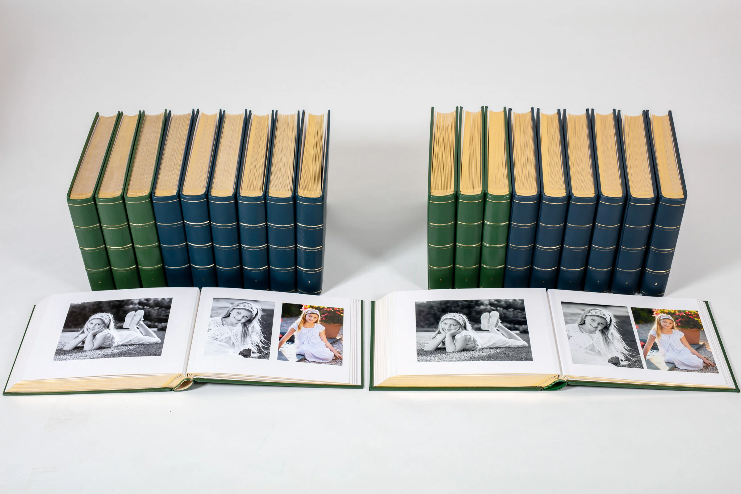 Open photo albums displaying photographs of a girl in a white dress and a girl lying on the grass, with additional closed photo albums behind them.