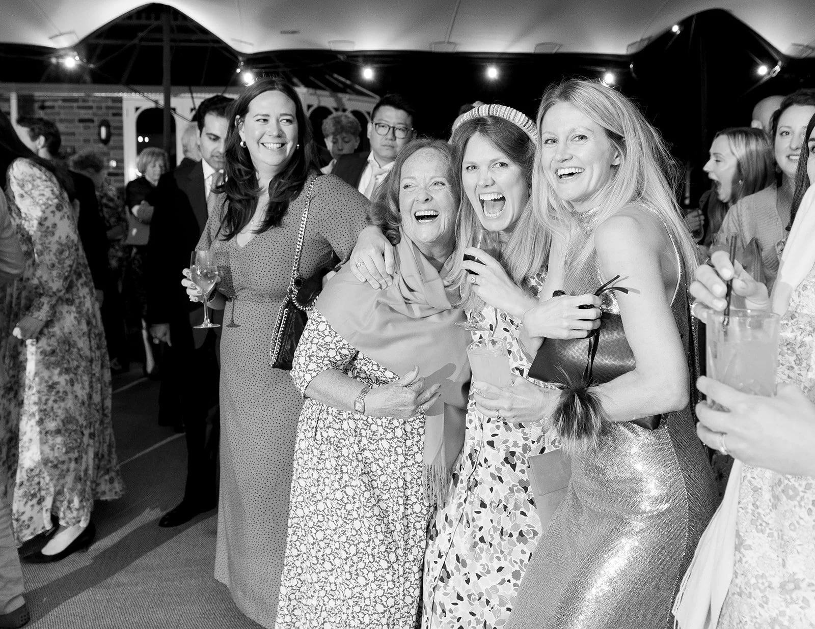 A group of women enjoying a celebration, smiling and laughing while holding drinks at a social gathering.