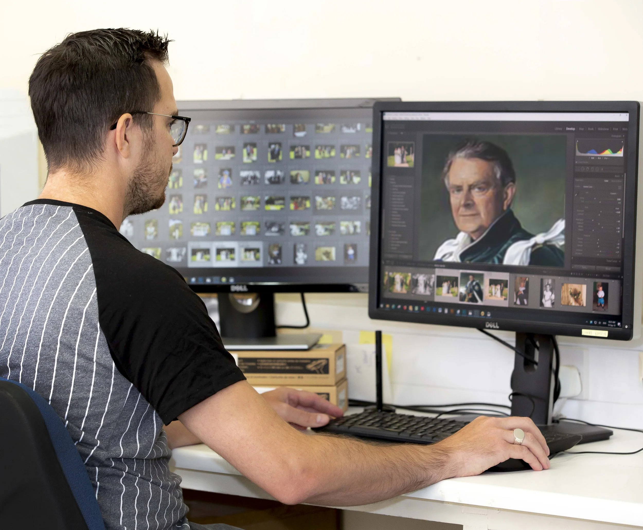 A man working on photo editing at his desk, viewing a portrait of a stern-looking elderly man on his computer monitor.
