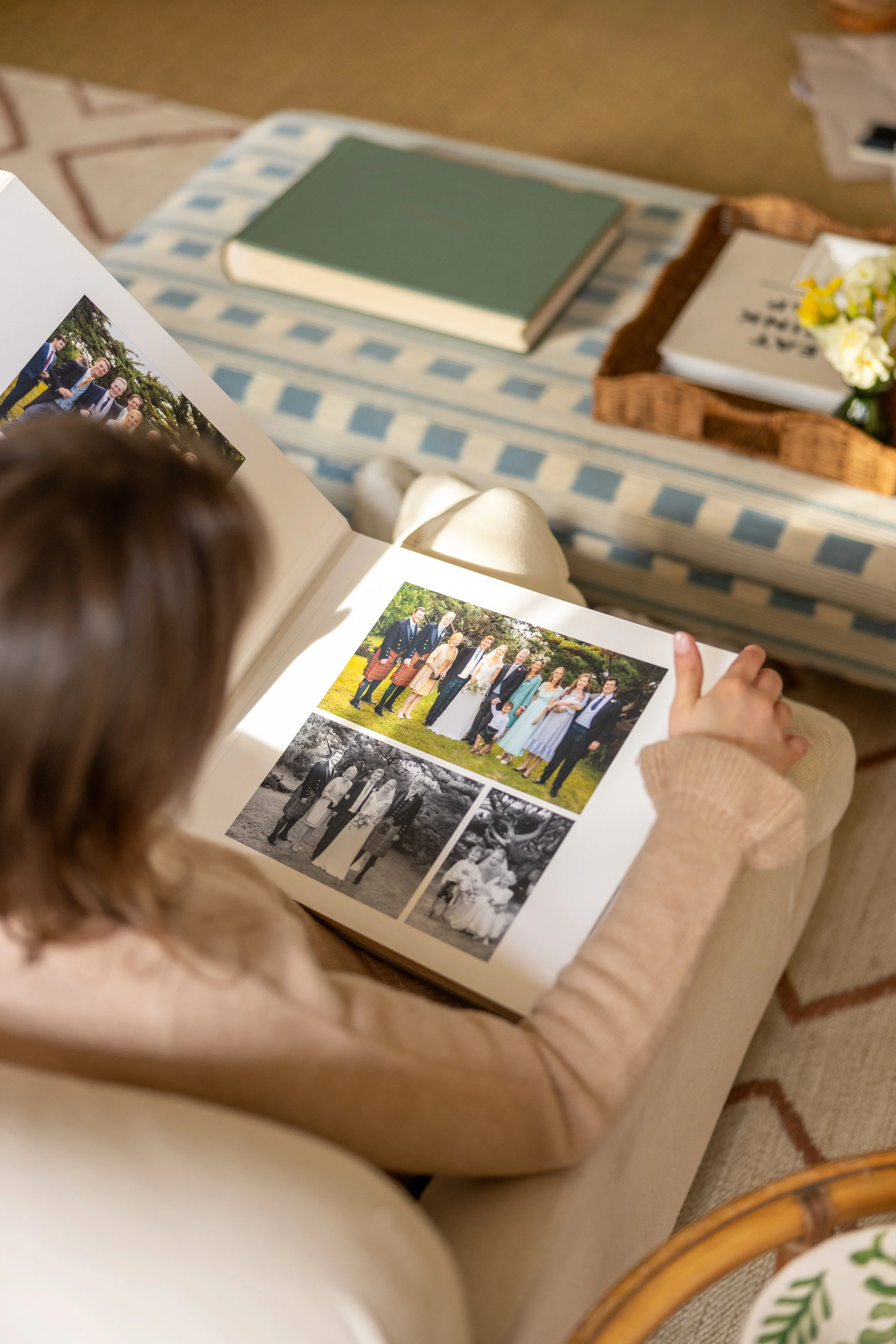 A young girl is looking at a photo album with black and white and color photographs of a group of people in formal and casual attire.
