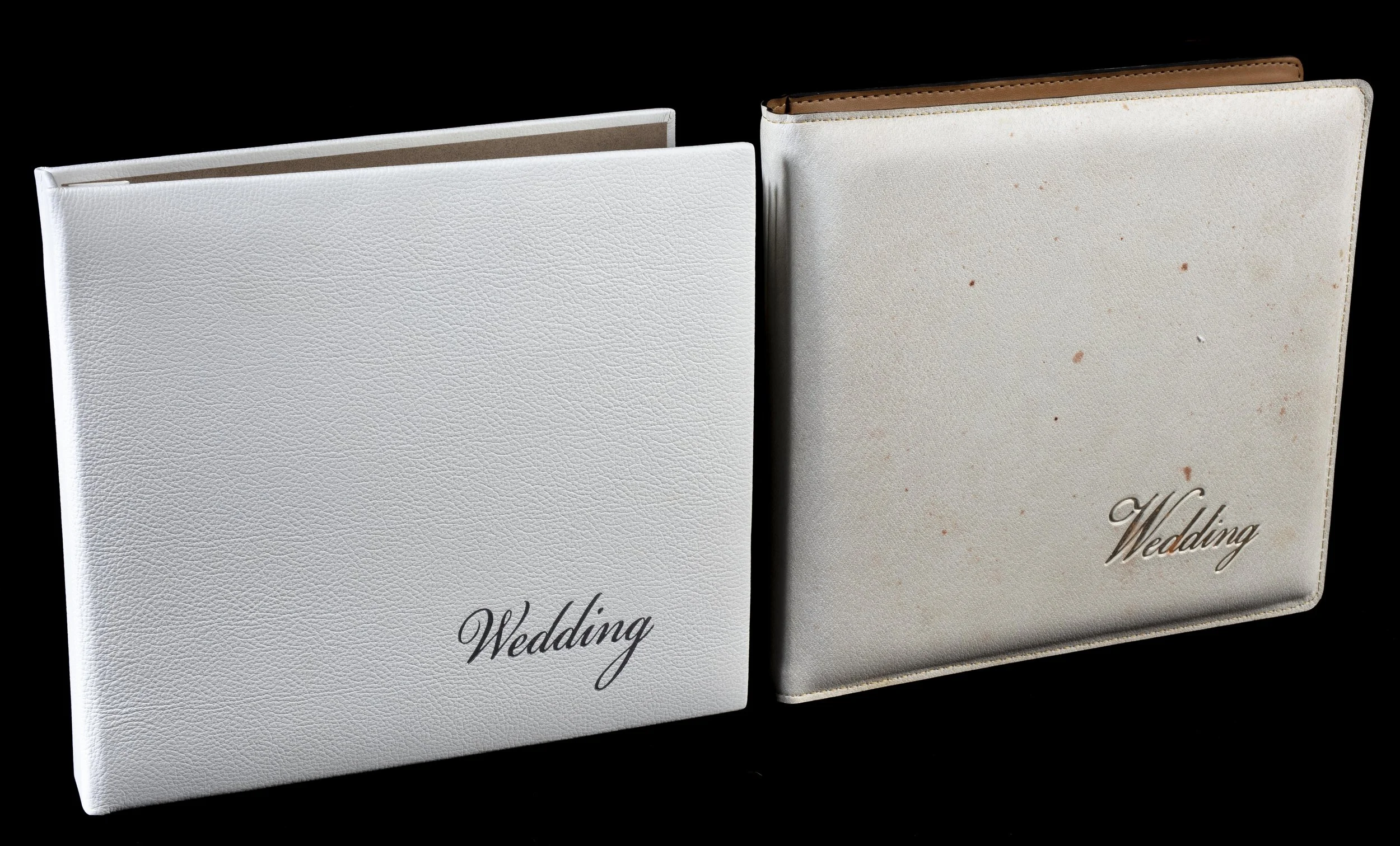 Two white wedding photo albums with the word 'Wedding' on the cover, one with a textured cover and the other with a plain cover, set against a black background.