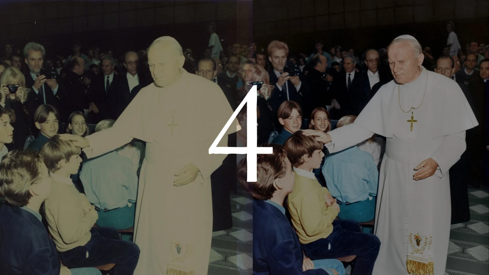 Pope John Paul II meeting children in an indoor event, with a crowd of adults and photographers in the background.