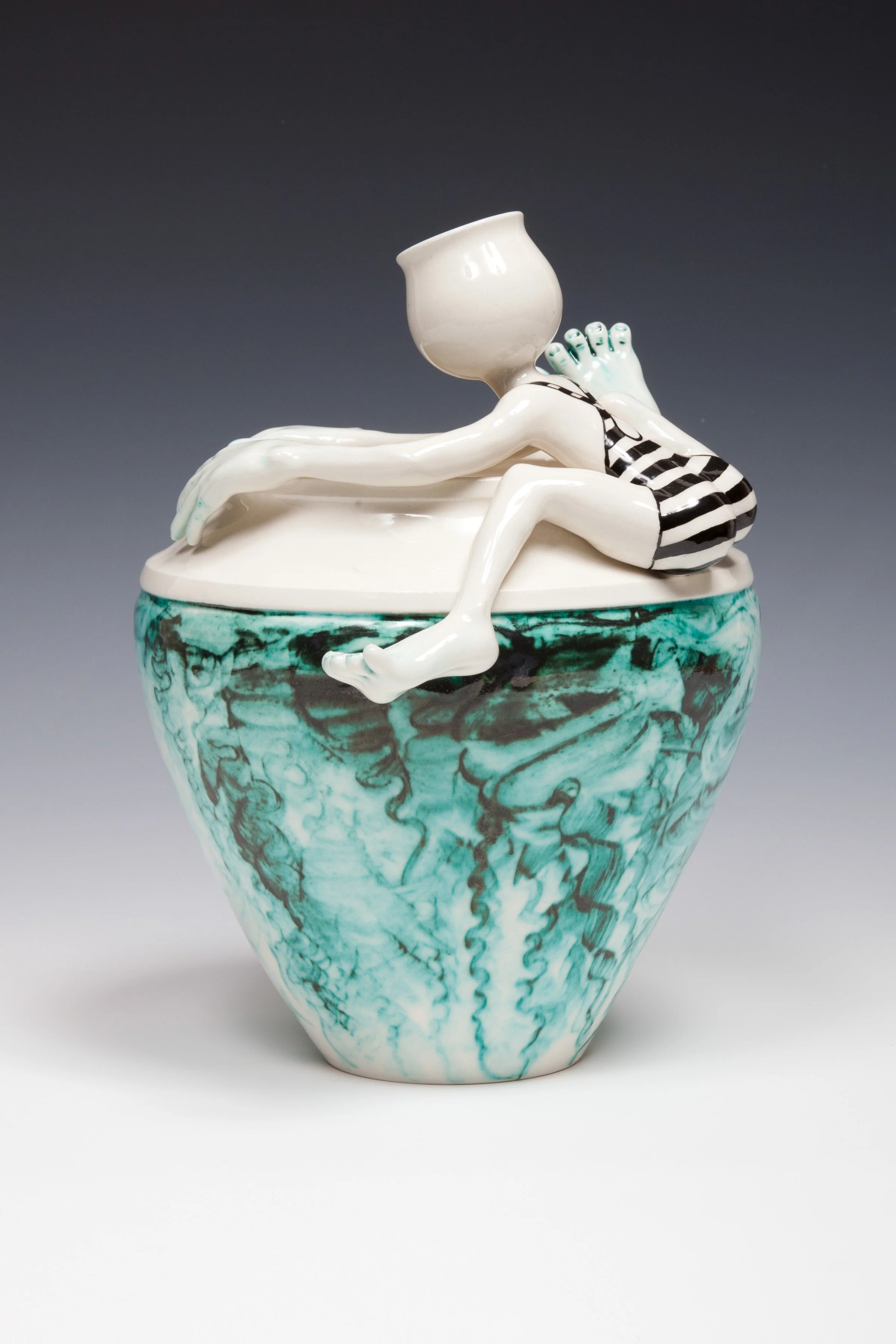 A ceramic sculpture of a person in striped swimwear leaning over the edge of a container, with their head replaced by a cup. The container has a marbled teal and white pattern.