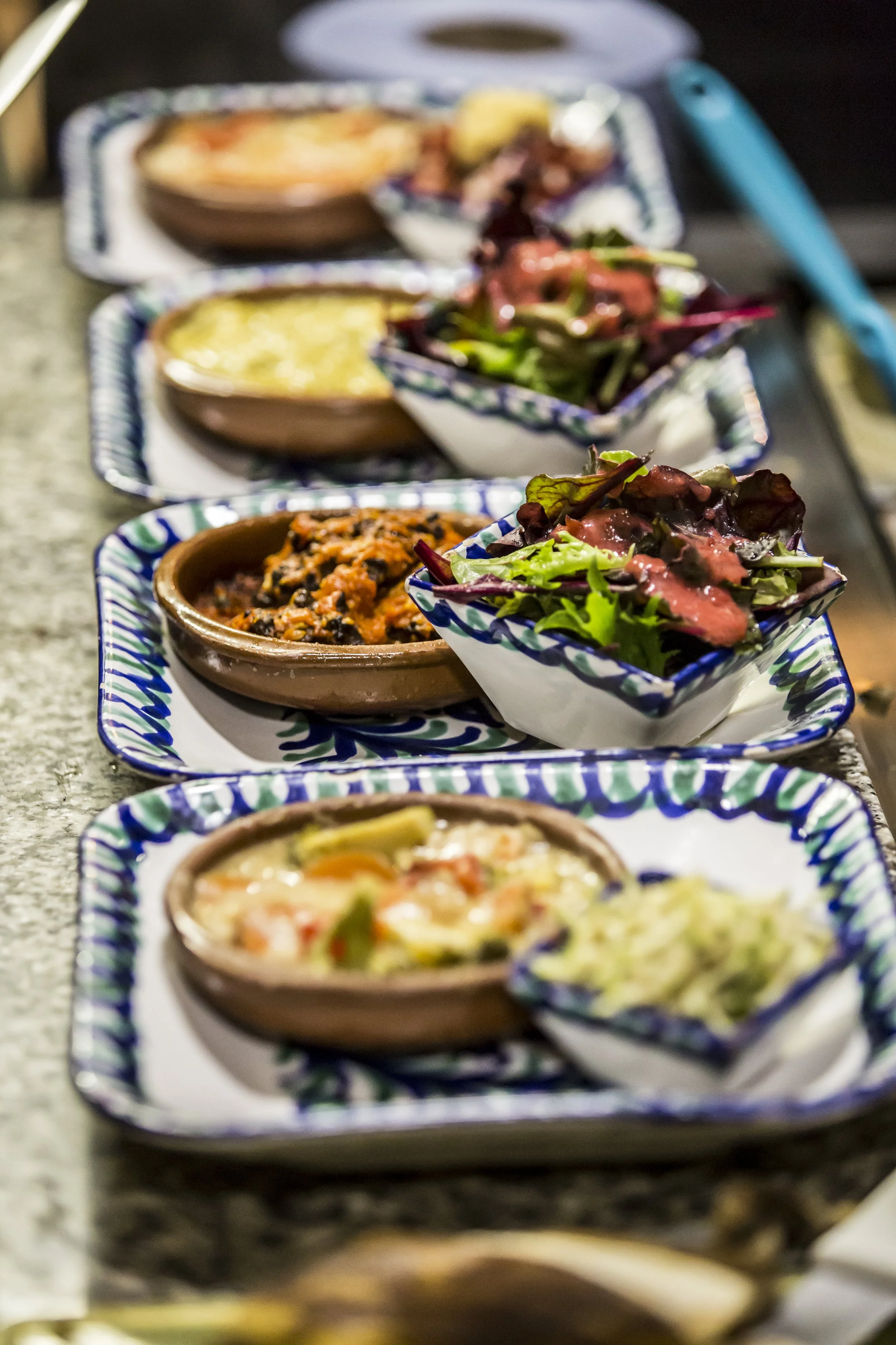Assorted Mexican dishes on a counter, including bowls of salad, salsa, black beans, and a casserole.