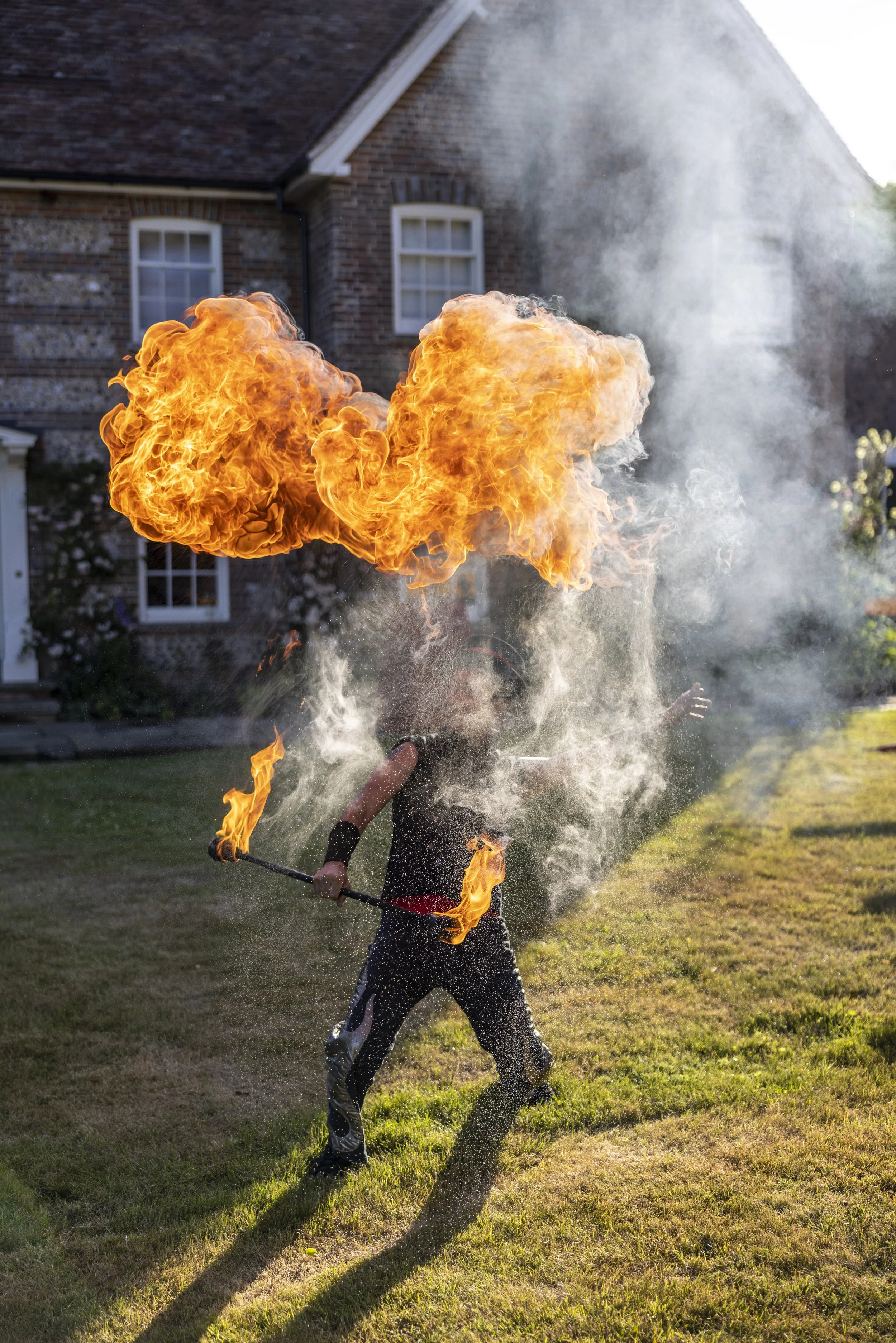 A person performing a fire breathing stunt outdoors, creating a large flame with fire breathing apparatus.