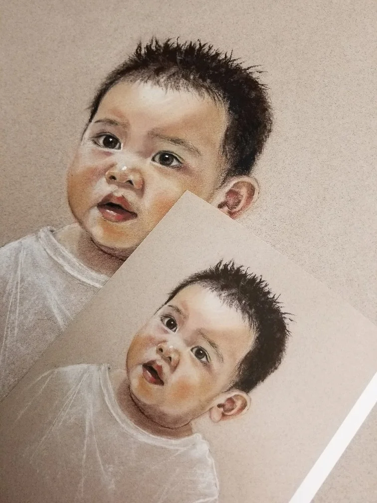 Printed photograph of a baby with dark, spiky hair and a curious expression, placed on a beige background.