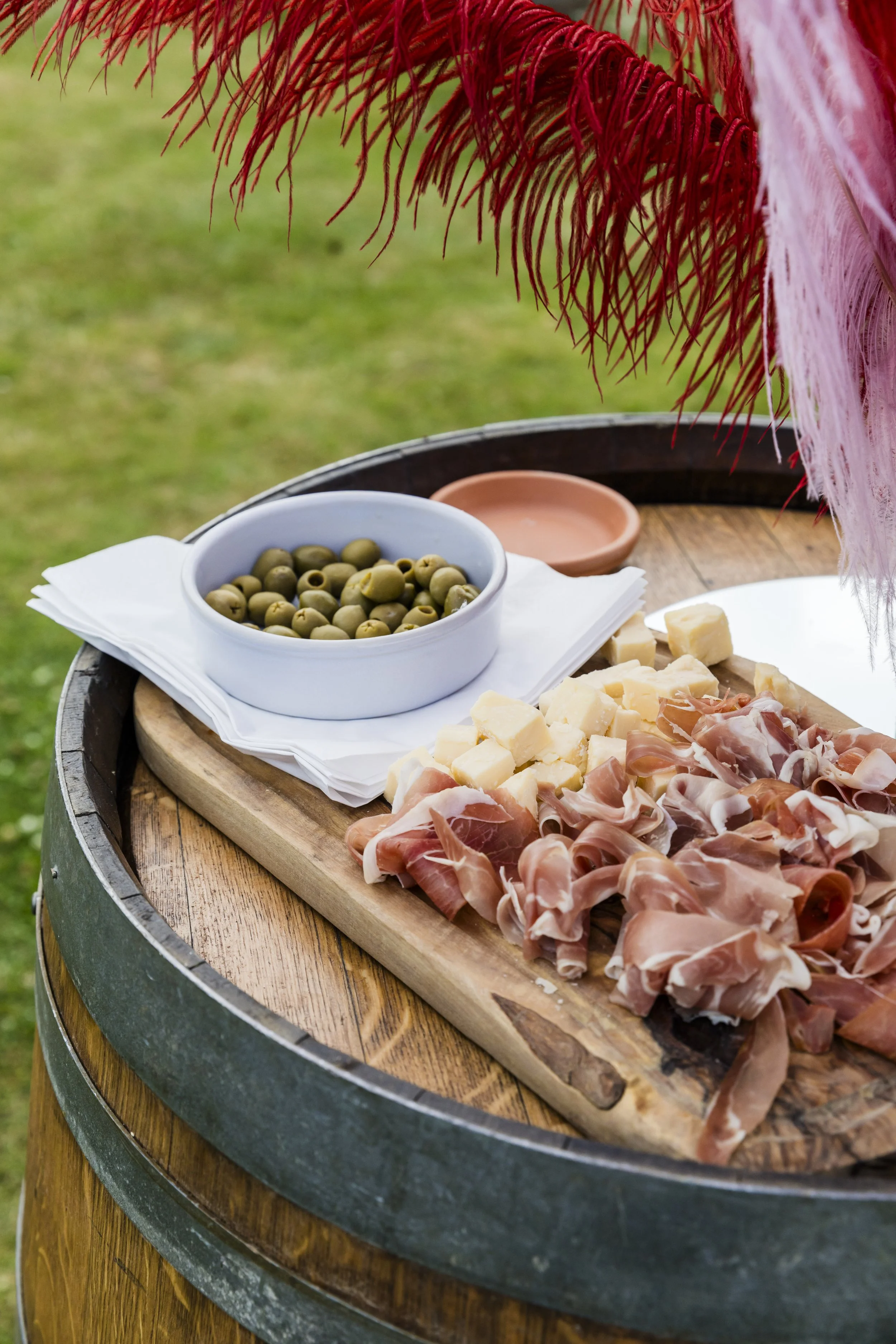 Charcuterie board with olives, cheese, and cured meat on a wooden barrel table, outdoors.