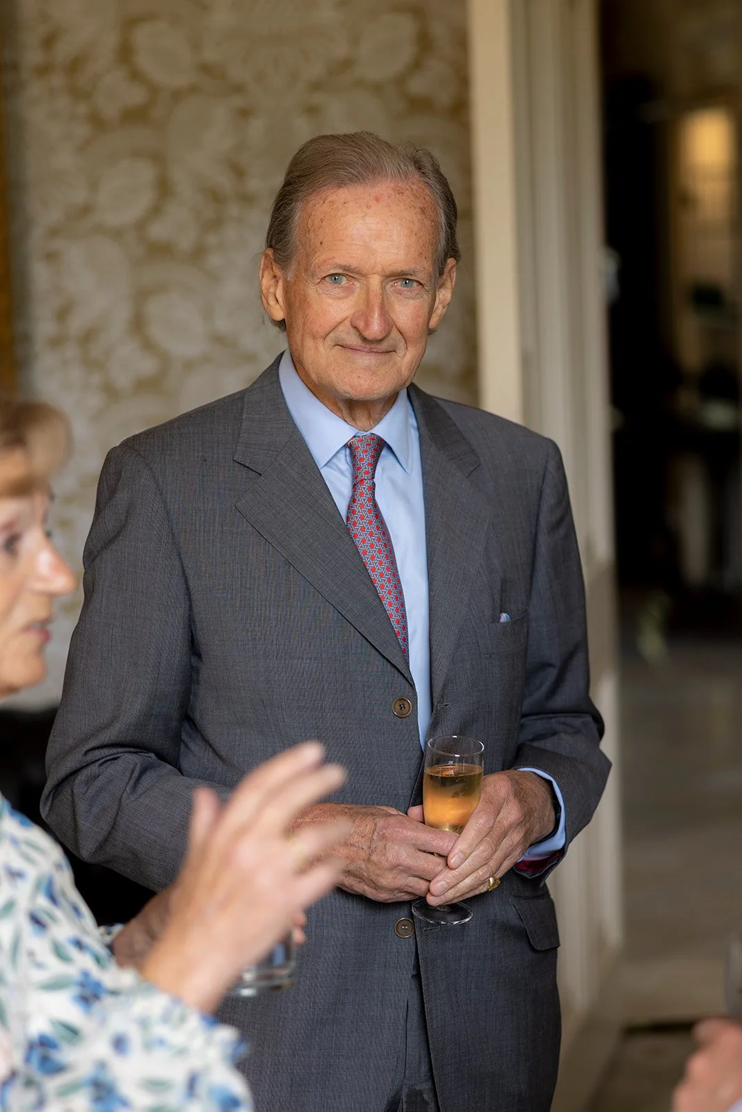 Older man in a gray suit holding a glass of champagne at a social gathering.