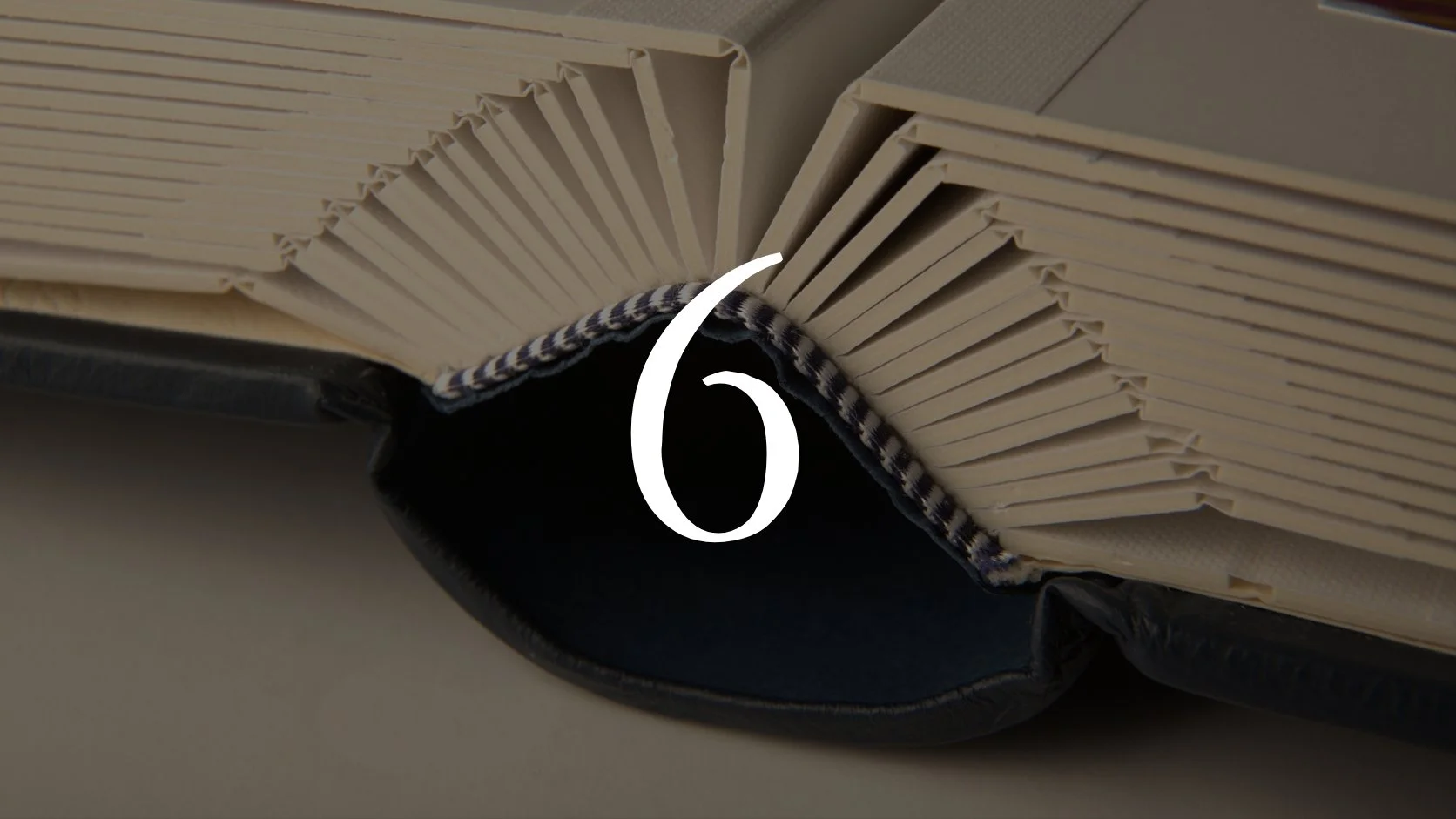 Close-up of an open book with a black cover, showing cream-colored pages held open by a black and white checkered fabric bookmark.