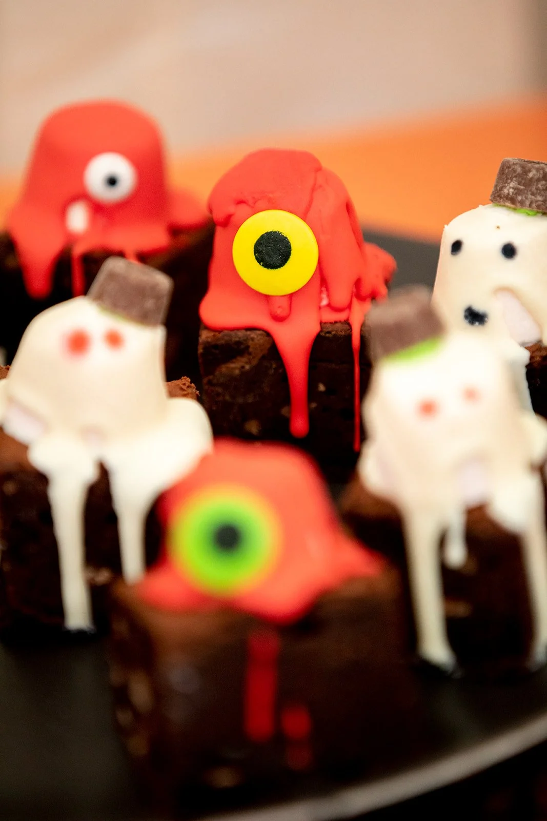 Halloween-themed chocolate cake decorated with ghost and monster fondant figures with colorful eyes and dripping red icing.