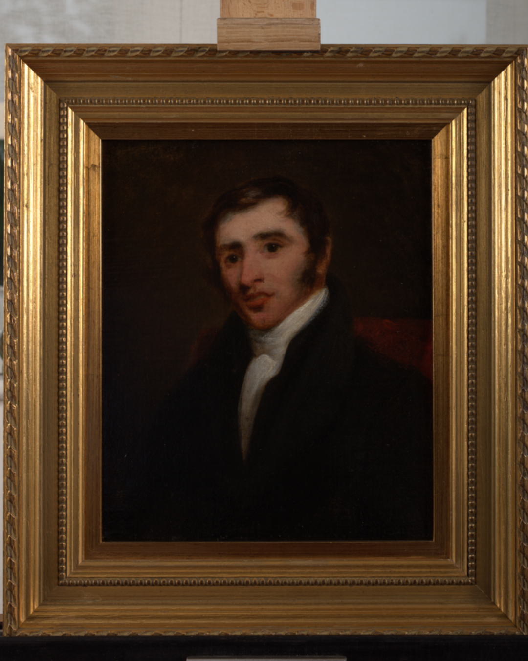 Portrait of a young man with dark hair, wearing a black coat and white shirt, in a gold ornate frame.