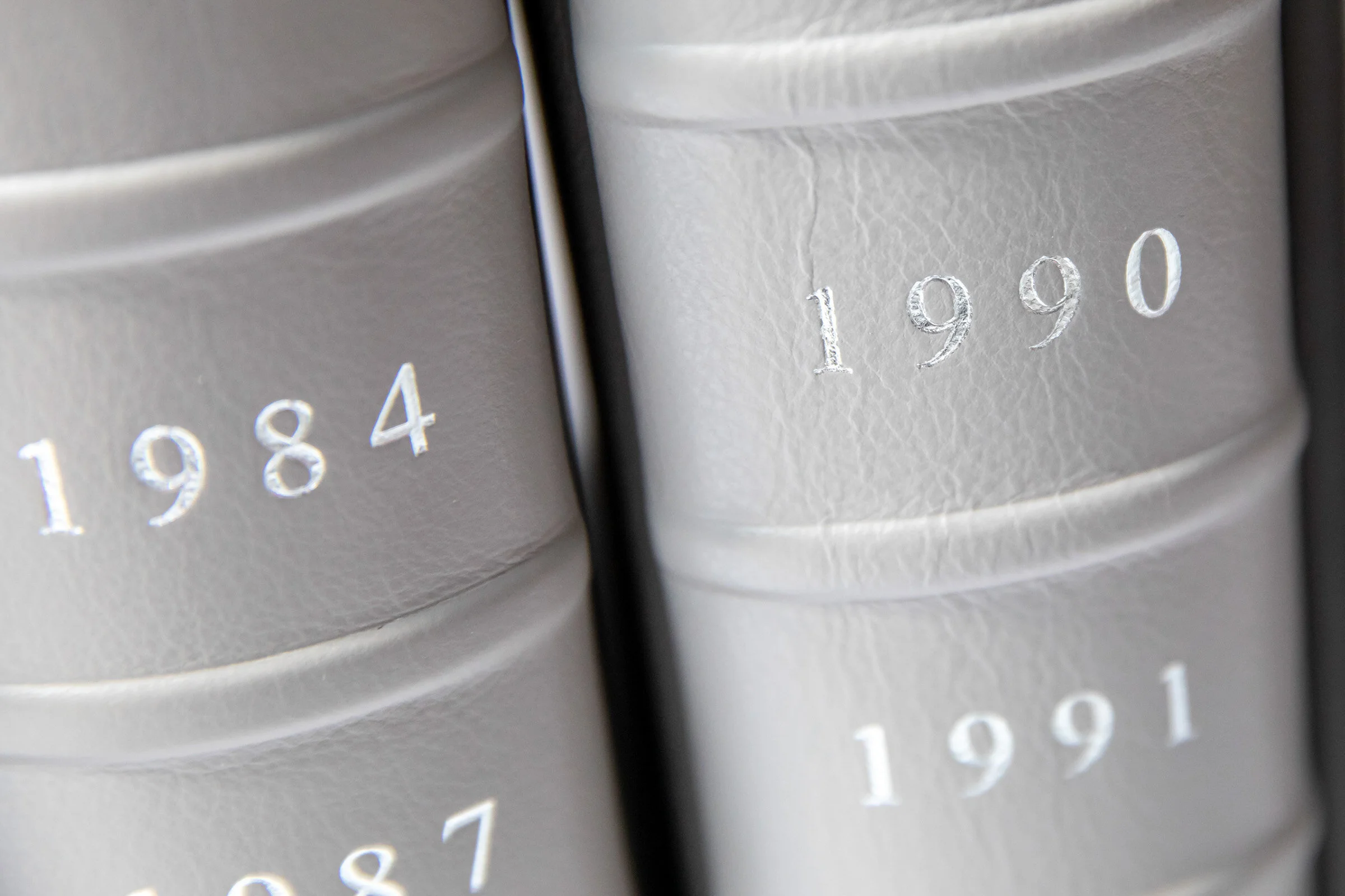 Close-up of beige leather-bound books with the years 1984, 1987, 1990, and 1991 embossed in silver on the spines.