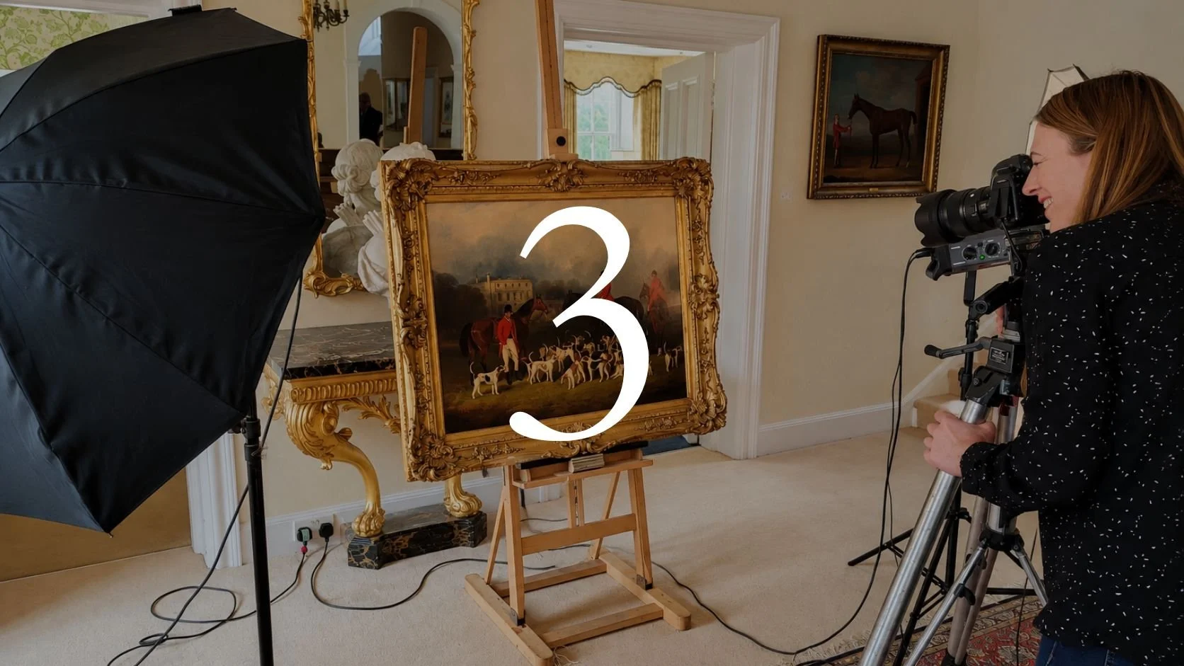 An art conservator is photographed inspecting a traditional painting mounted in an ornate gold frame, with a number 3 overlayed on the image. The scene appears to be in a well-lit, decorated room with a second artwork on the wall and plants reflected in a mirror.