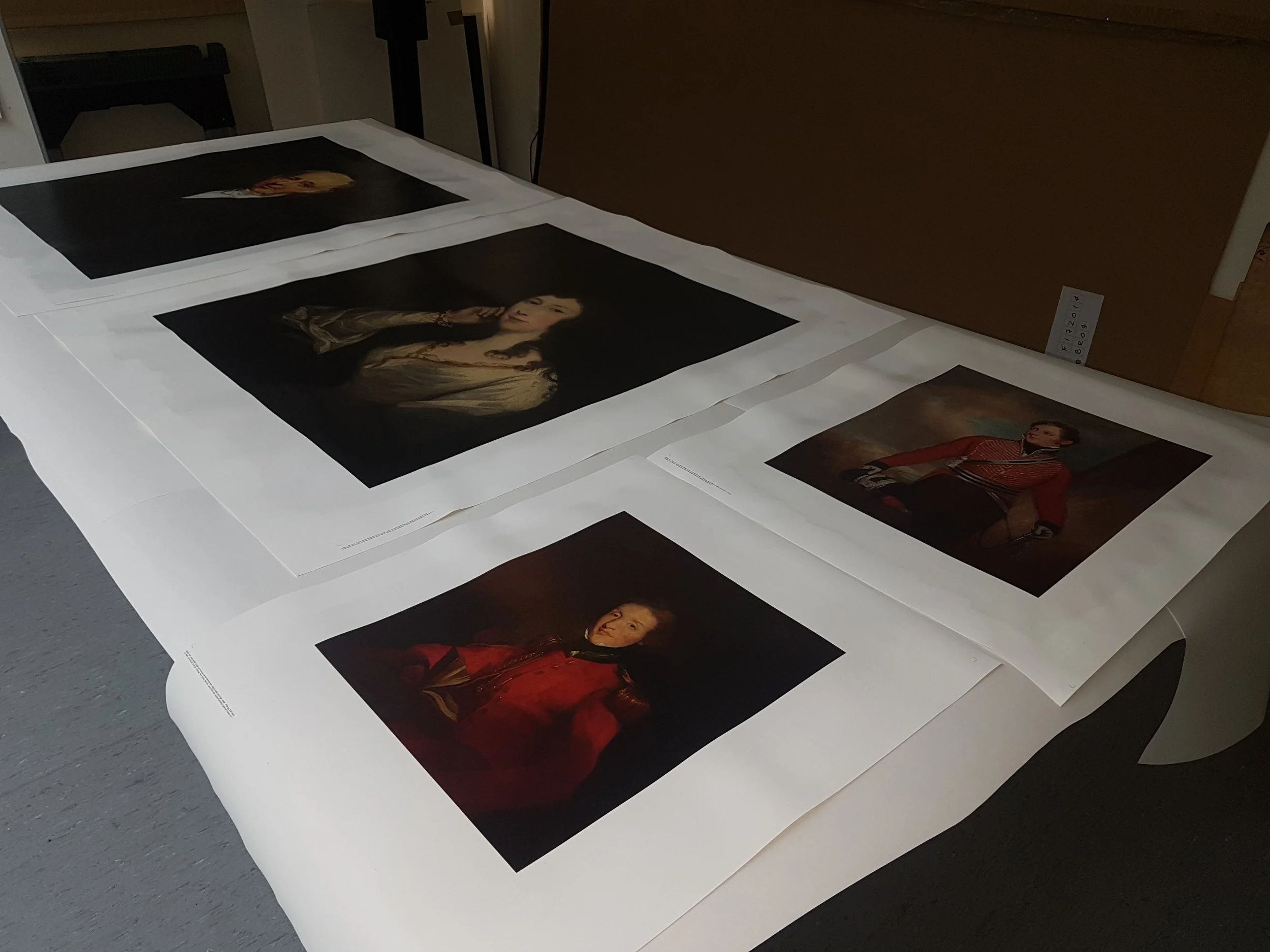 Printed portraits of historical figures laid out on a table, presumably for viewing or framing.